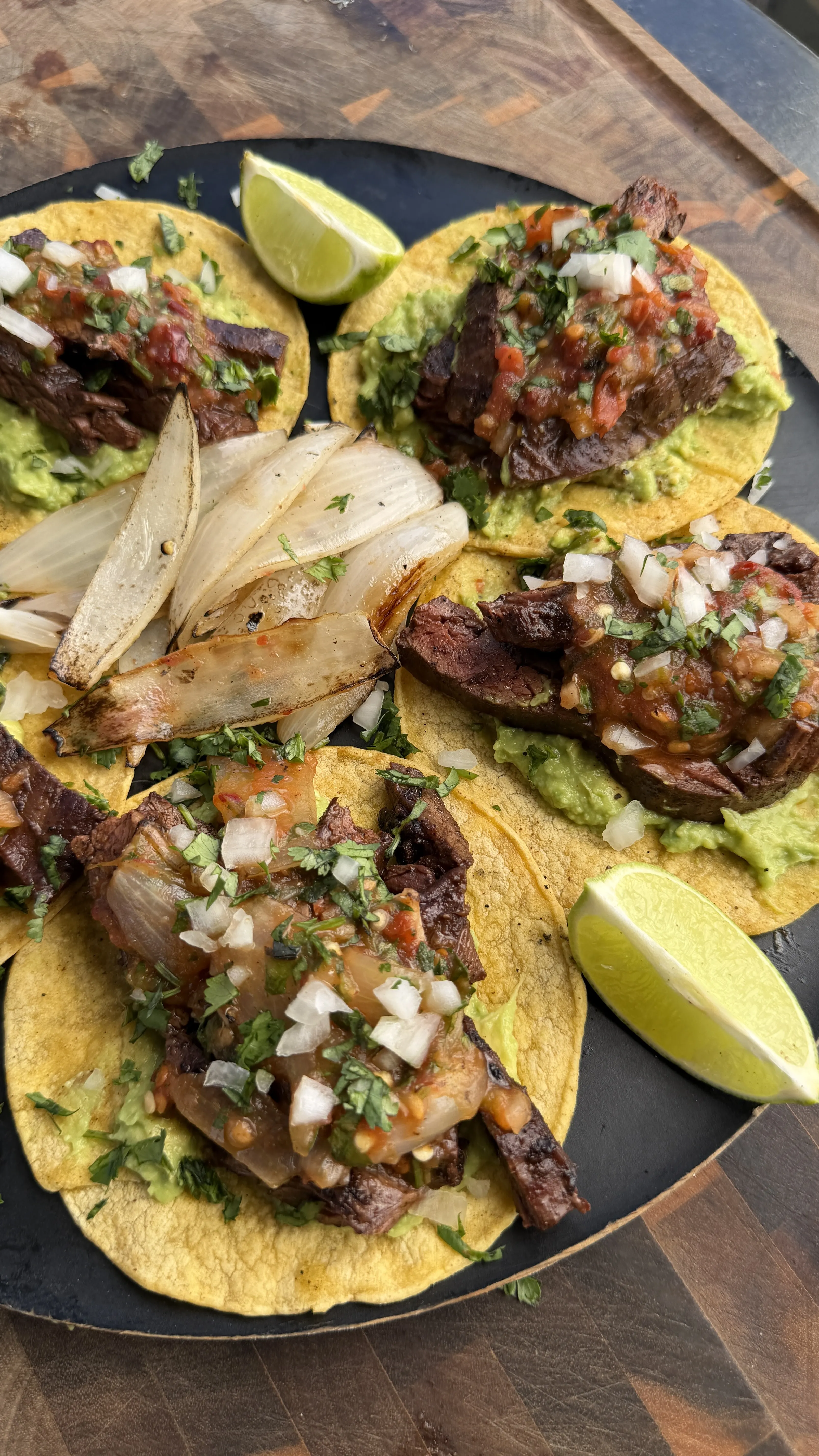 Four skirt steak tacos with chipotle salsa, guacamole, onions and cilantro on corn tortillas with lime wedges
