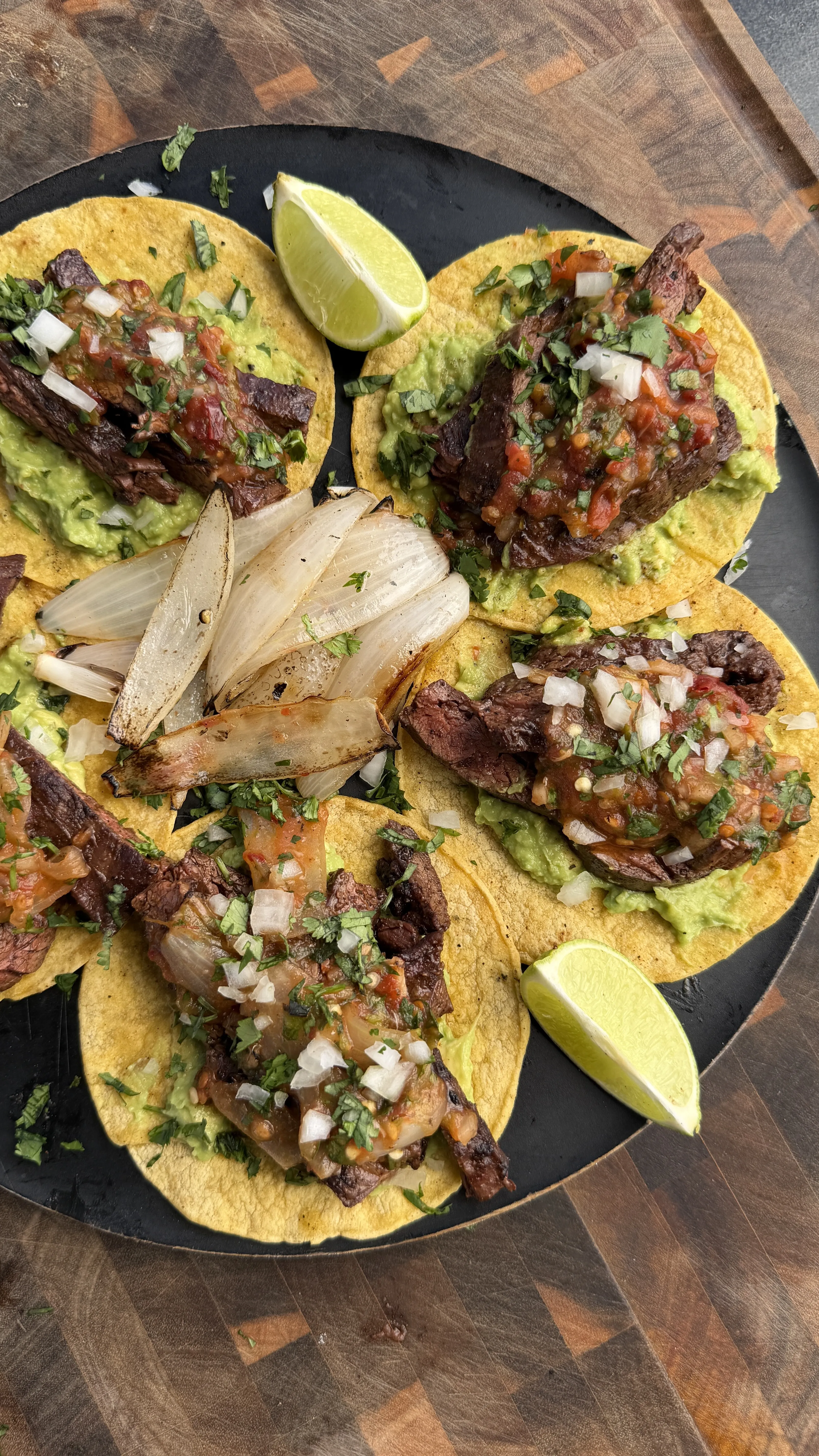Skirt steak tacos with chipotle salsa, grilled onions, and lime wedges arranged on a black plate