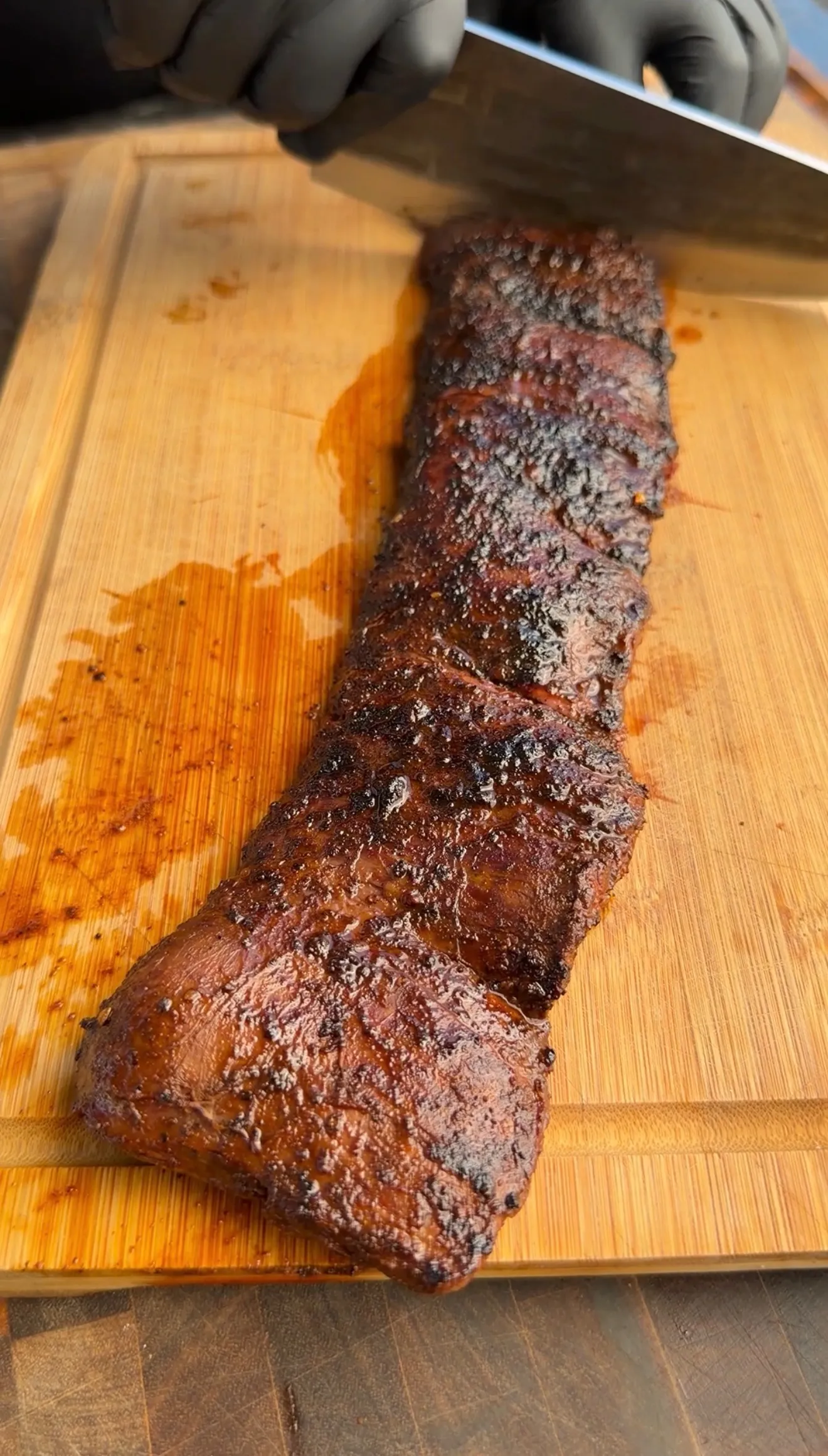Sliced grilled skirt steak with char marks on a wooden cutting board, being cut with a knife