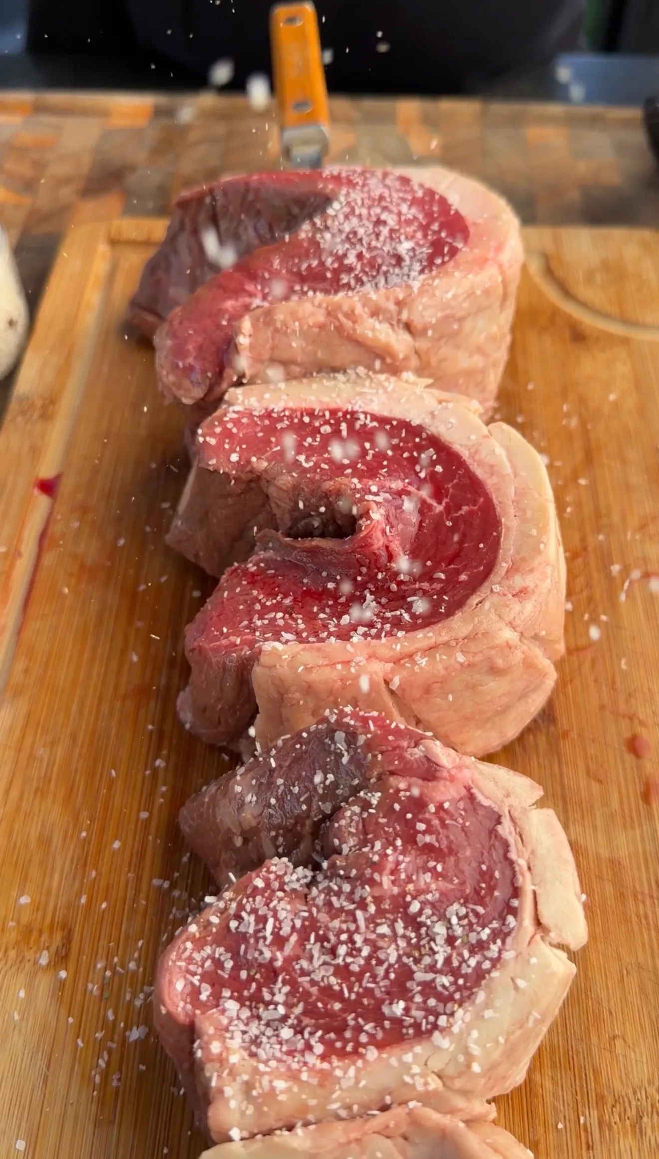 Thick slices of raw picanha steak seasoned with coarse salt on a wooden cutting board