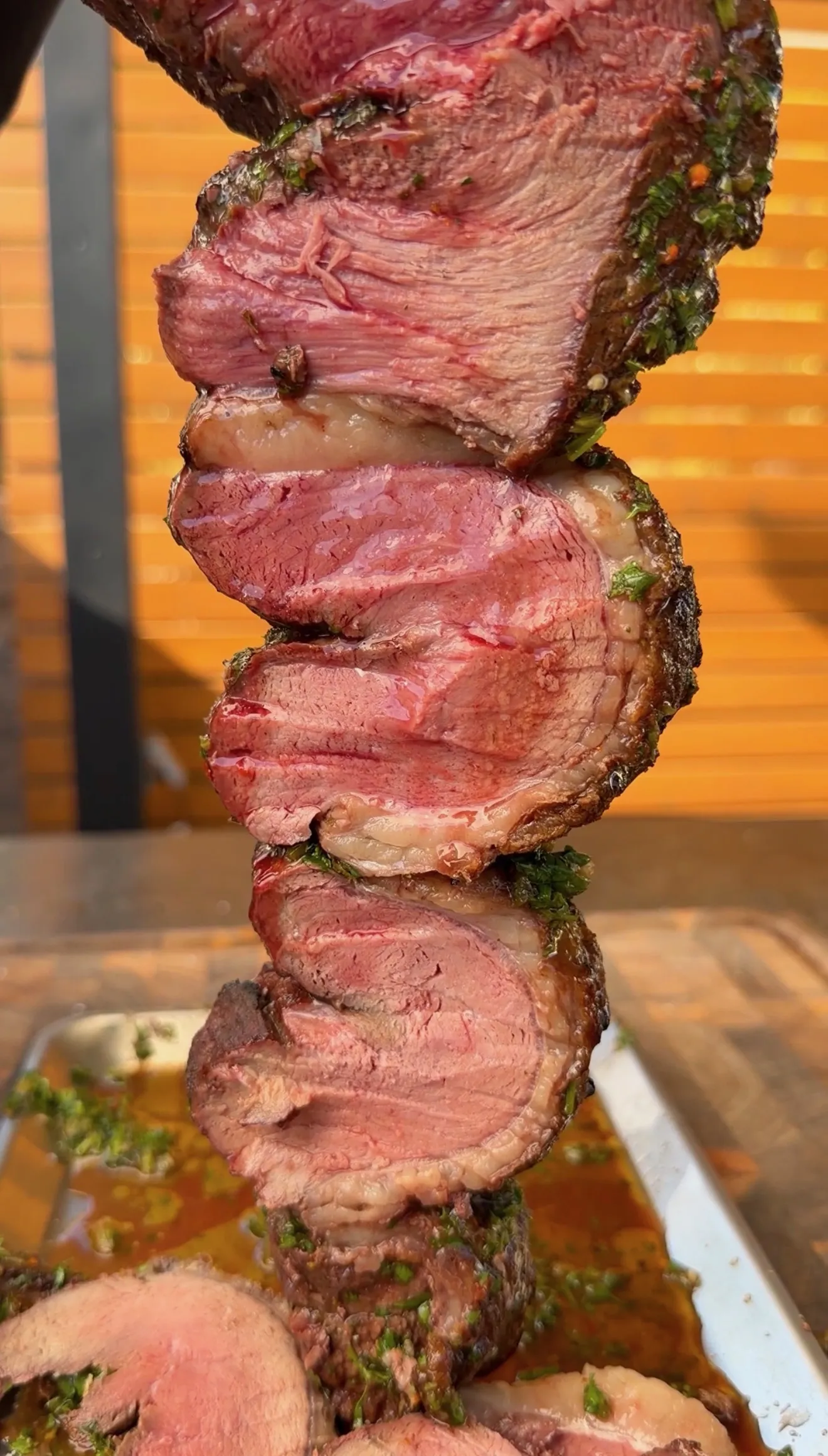 Sliced medium-rare picanha steak with green jalapeño chimichurri sauce being carved with knife