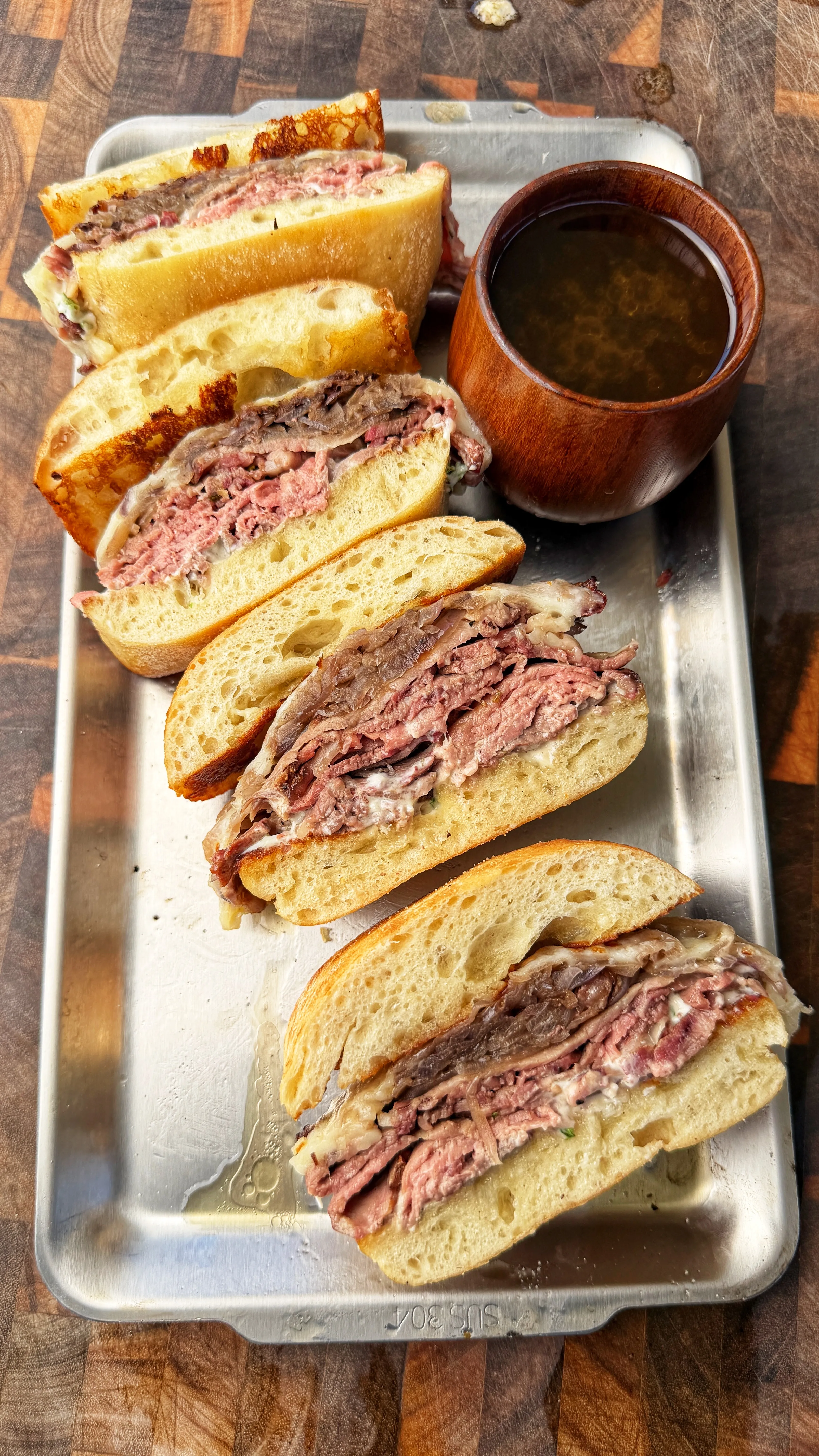 Sliced garlic herb butter smoked prime rib French dip sandwiches on metal tray with au jus dipping sauce