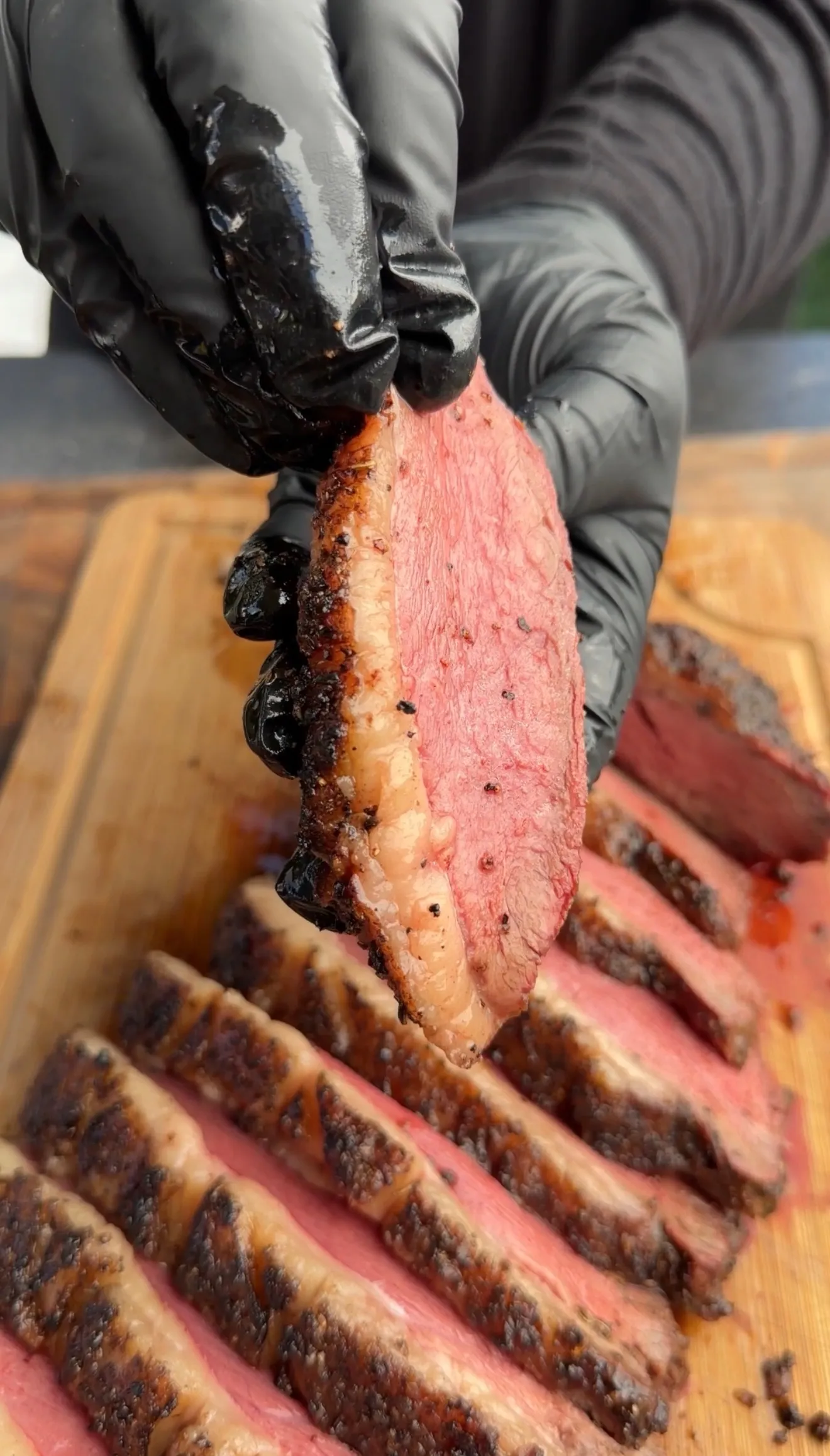 Sliced smoked picanha roast showing pink medium-rare interior with charred crust being held by gloved hands