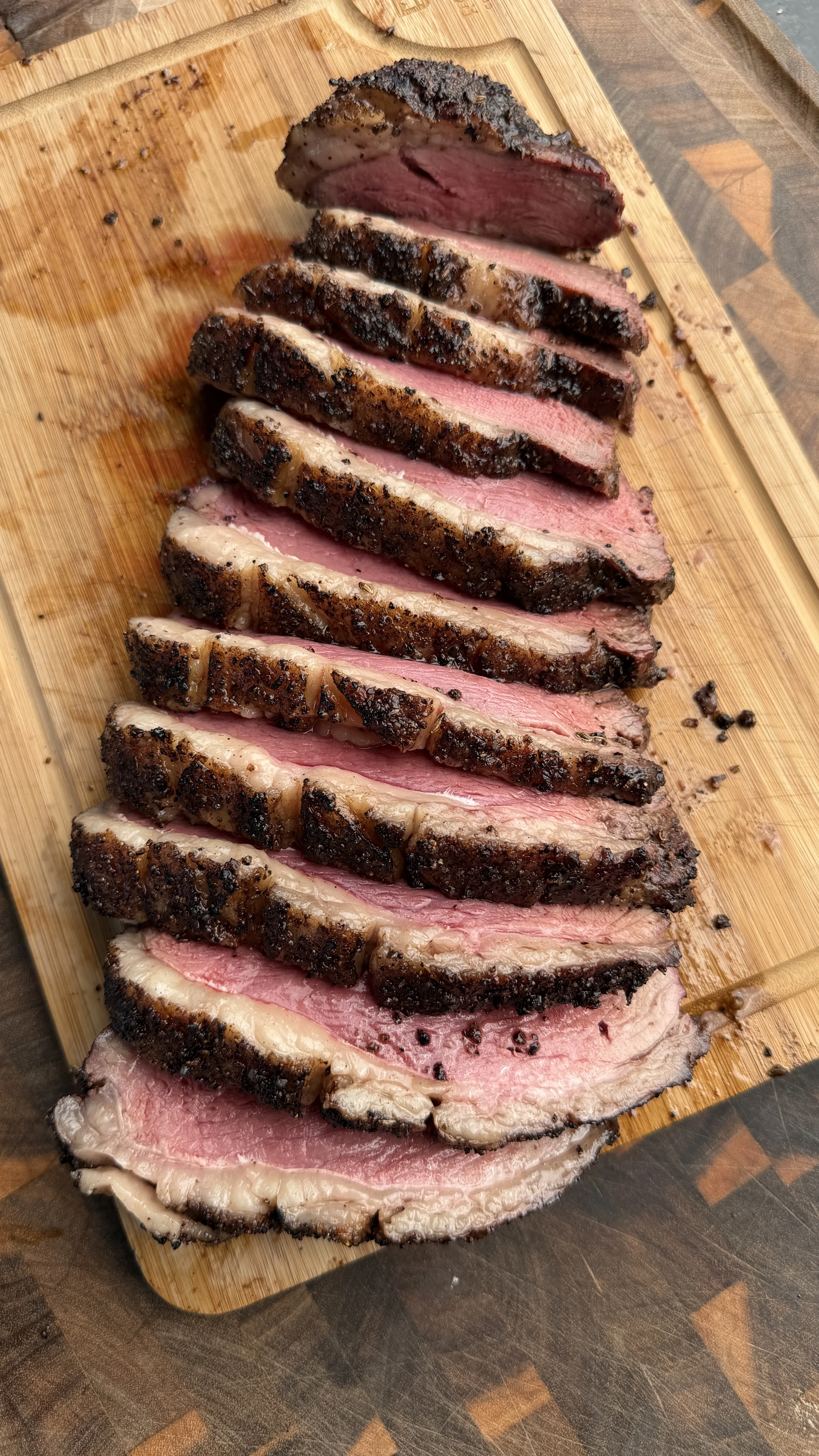 Sliced smoked picanha roast with dark crust showing pink interior on wooden cutting board