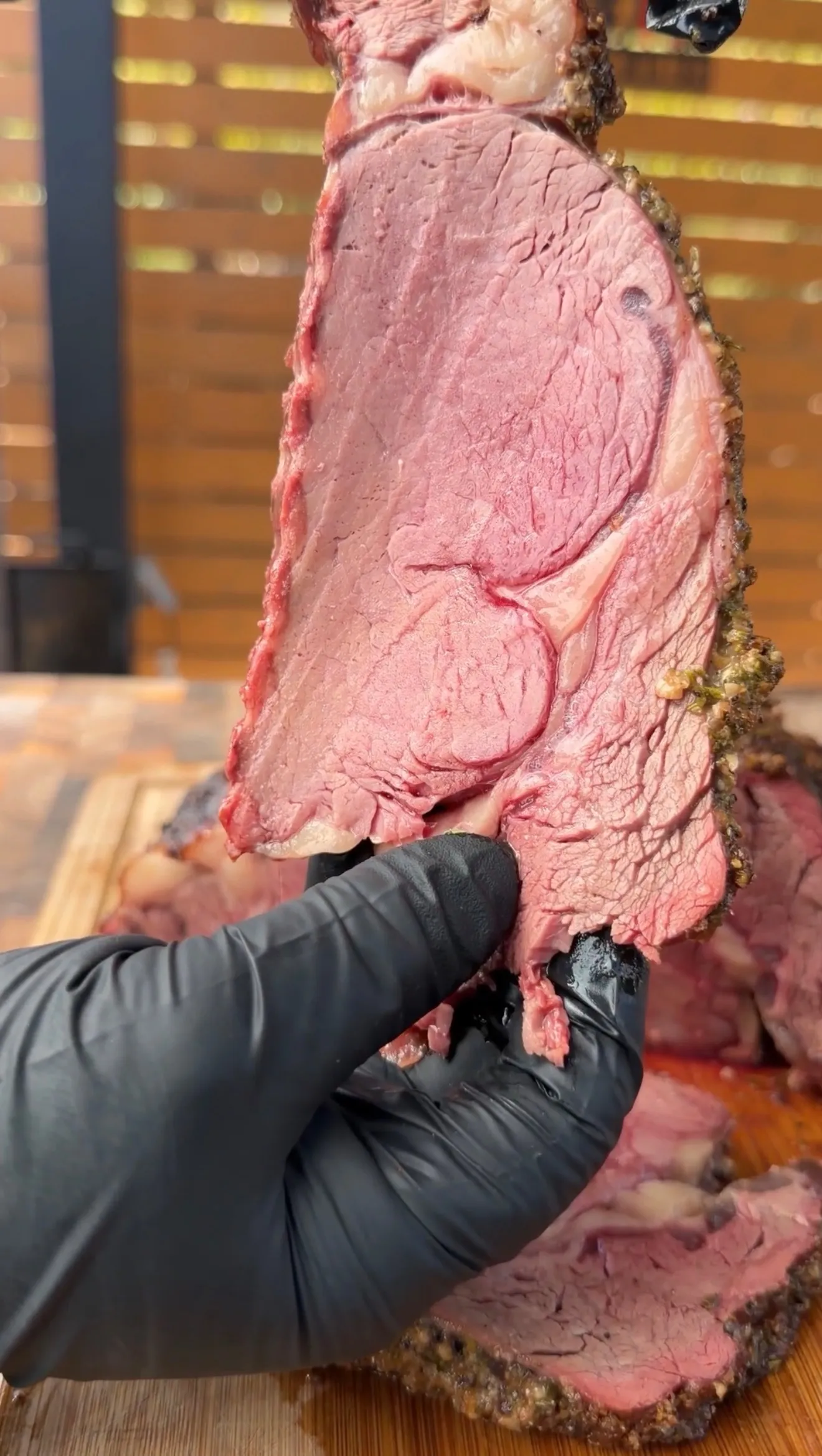 Hand in black glove slicing perfectly smoked prime rib with pink interior and dark seasoned crust