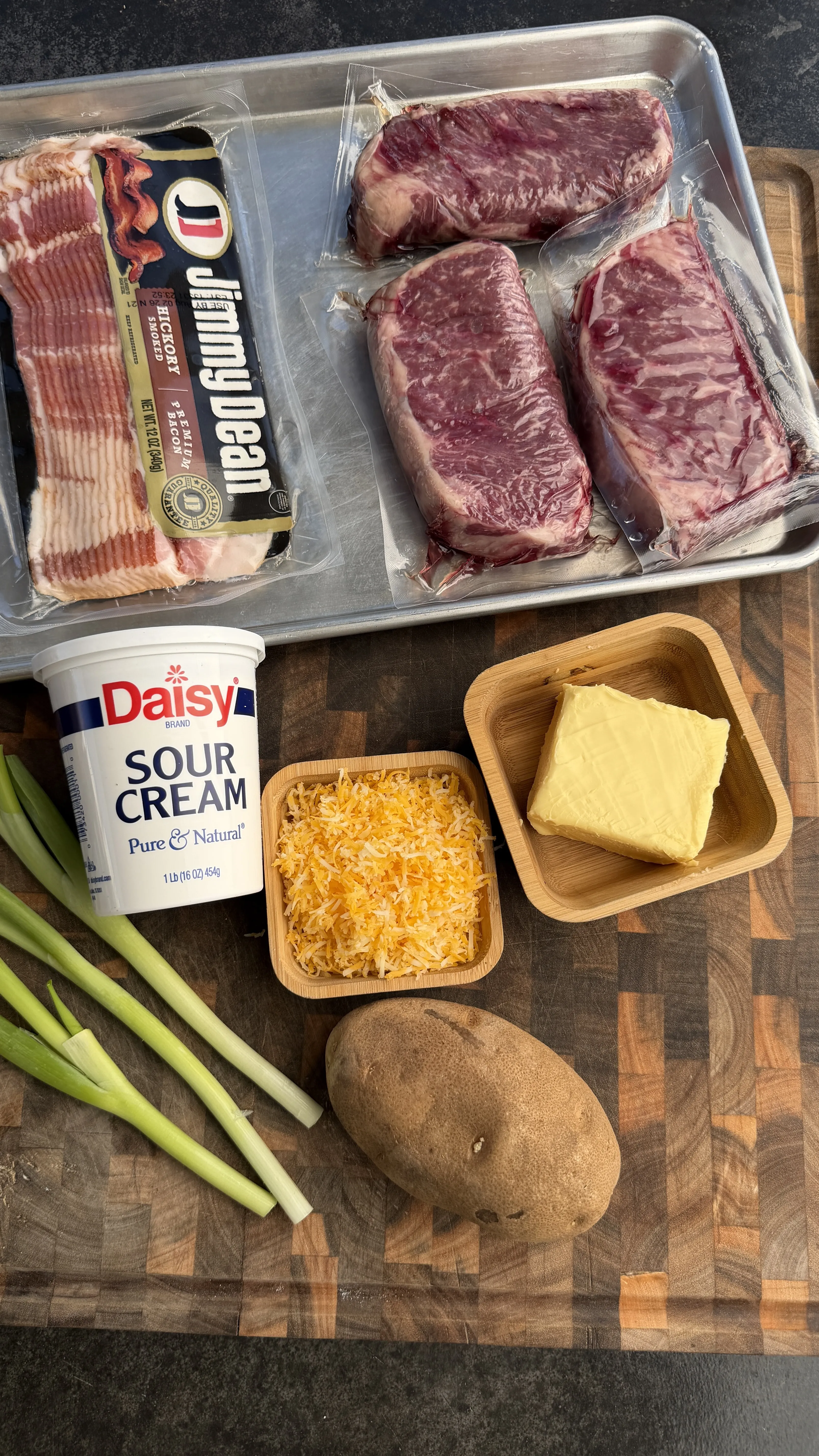 Ingredients for smashed steak loaded potatoes: NY strip steaks, bacon, sour cream, shredded cheese, butter, potato, and green onions
