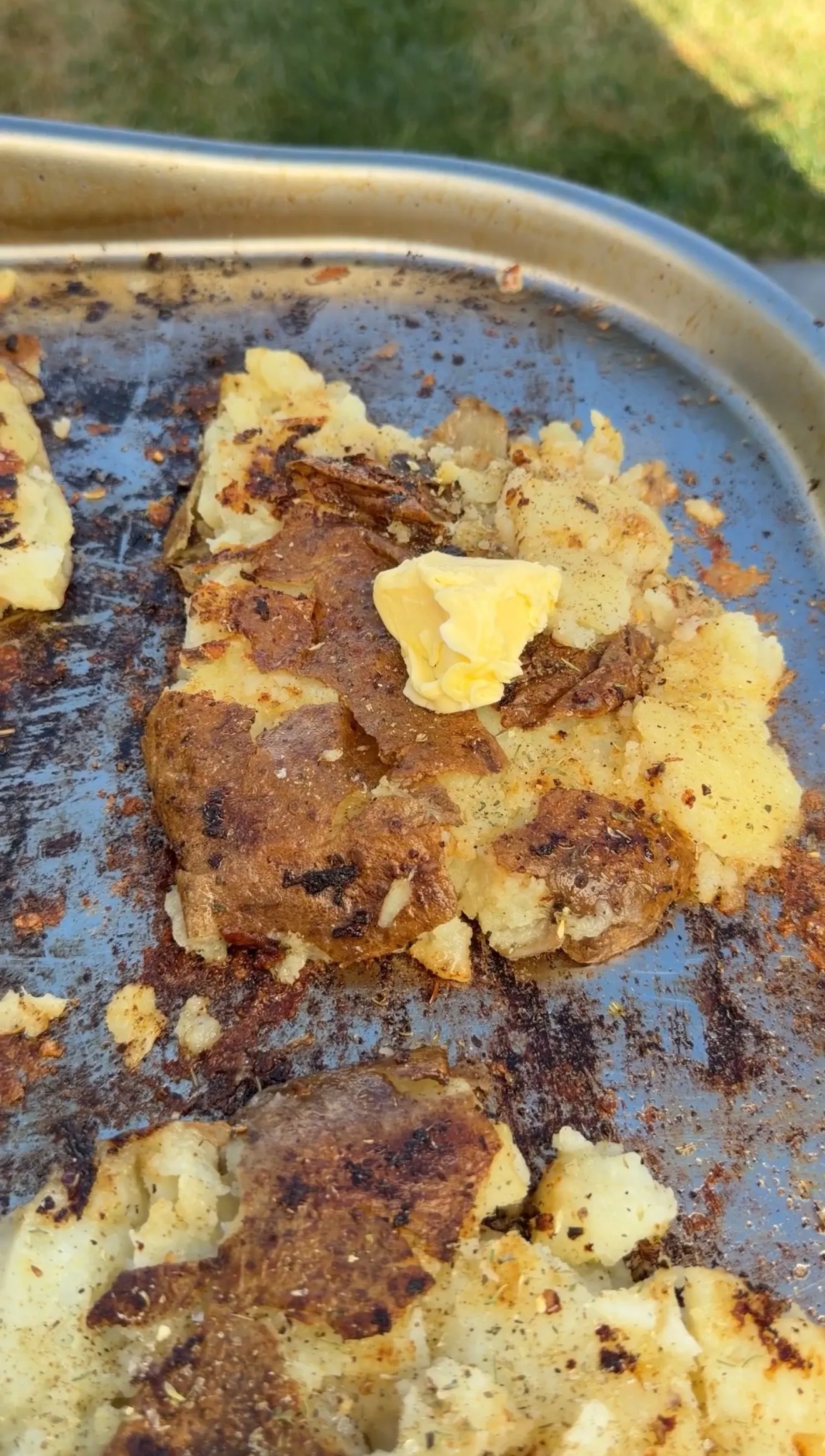 Crispy smashed loaded potato topped with seasoned steak and a pat of melting butter on a baking sheet