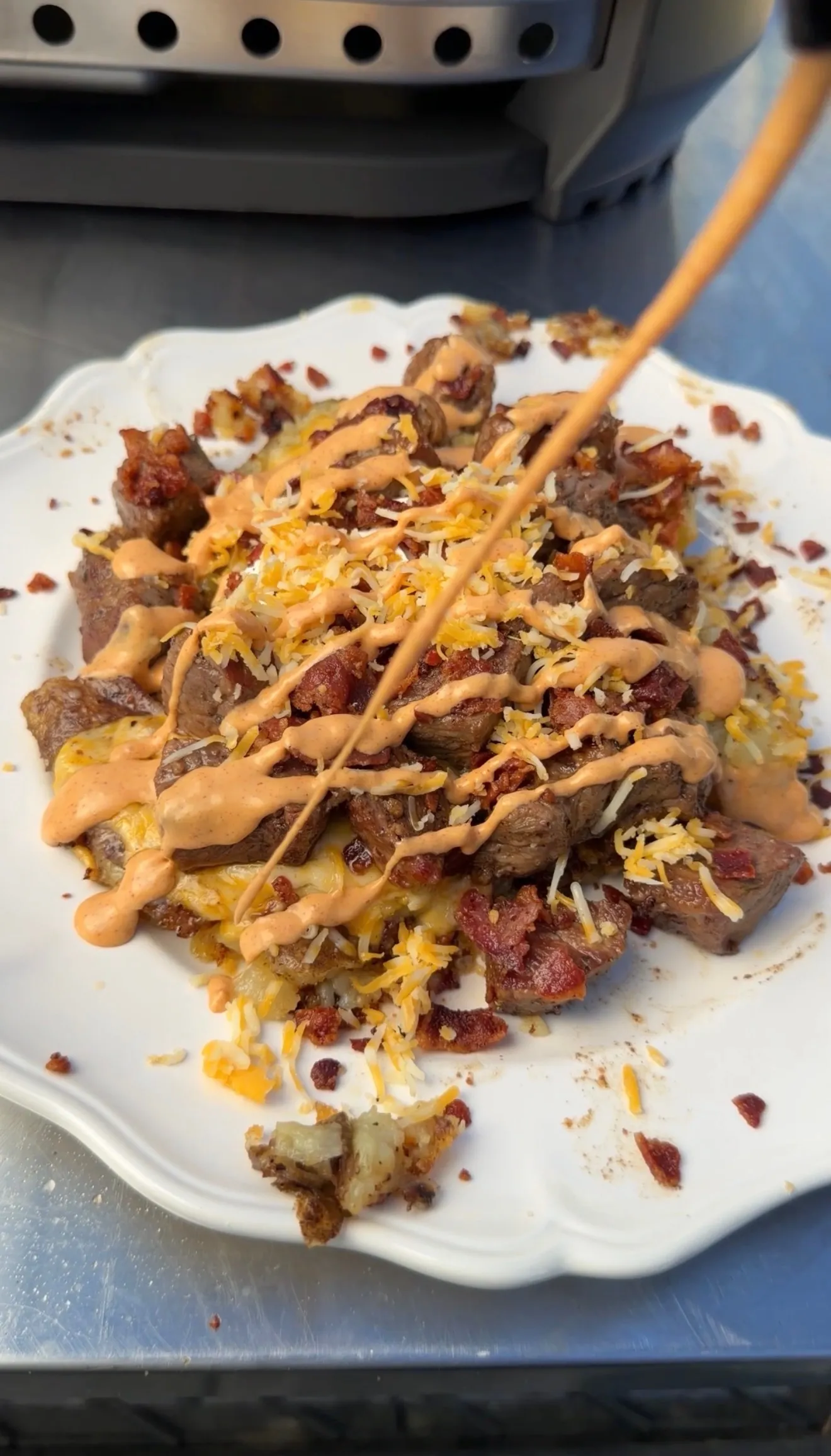 Smashed steak loaded potatoes topped with shredded cheese, crispy bacon, and creamy chipotle sauce drizzle on white plate