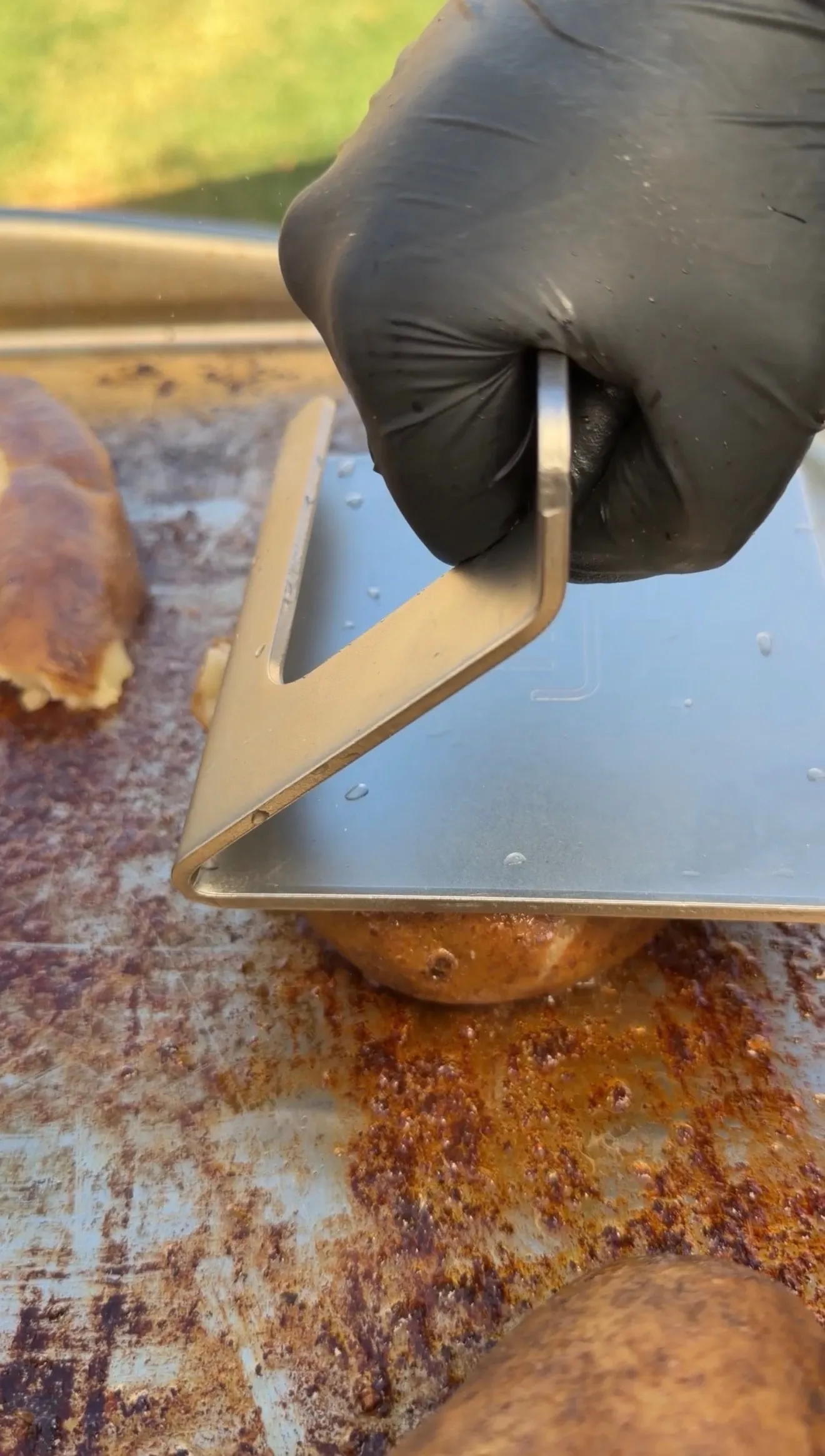 Black-gloved hand pressing a burger smasher down on a potato on a seasoned flat top griddle