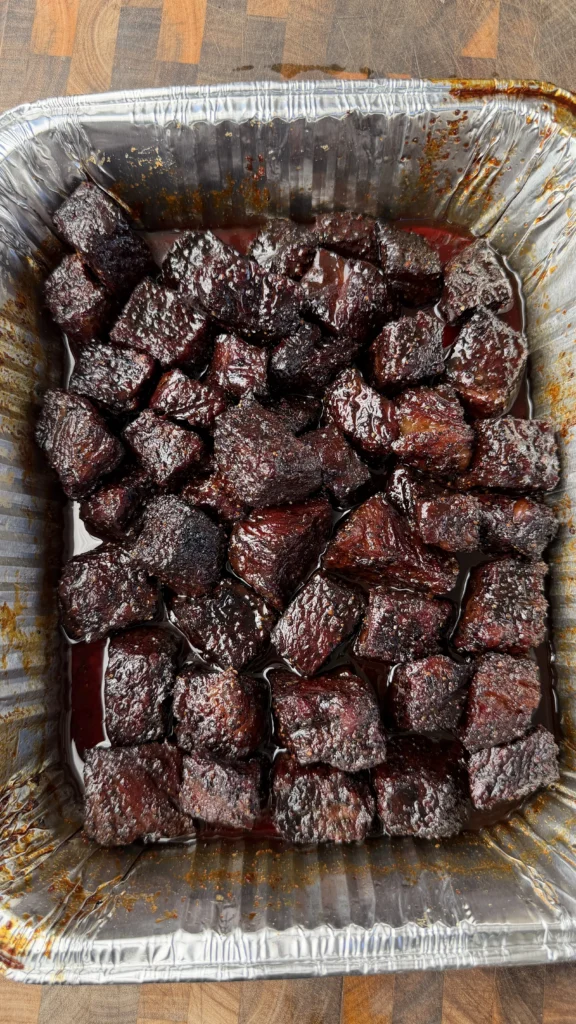 Glazed smoked beef rib burnt ends in aluminum foil pan with dark molasses coffee coating
