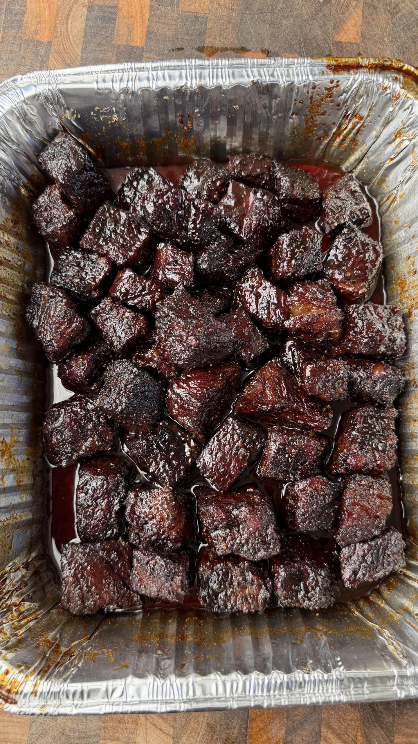 Glazed smoked beef rib burnt ends in aluminum foil pan with dark molasses coffee coating