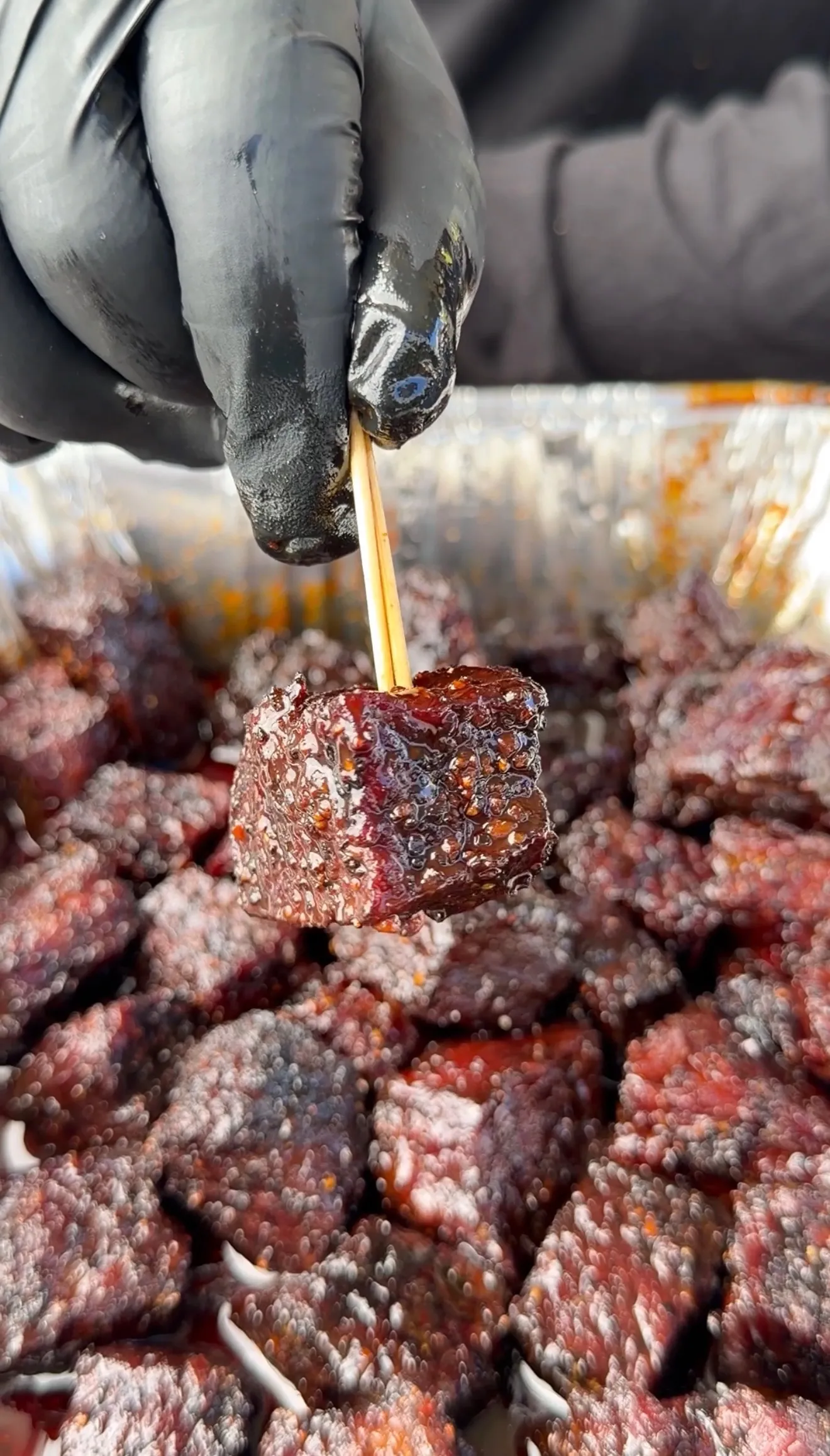 Gloved hand brushing molasses glaze onto cubed smoked beef rib burnt ends with glossy caramelized surface