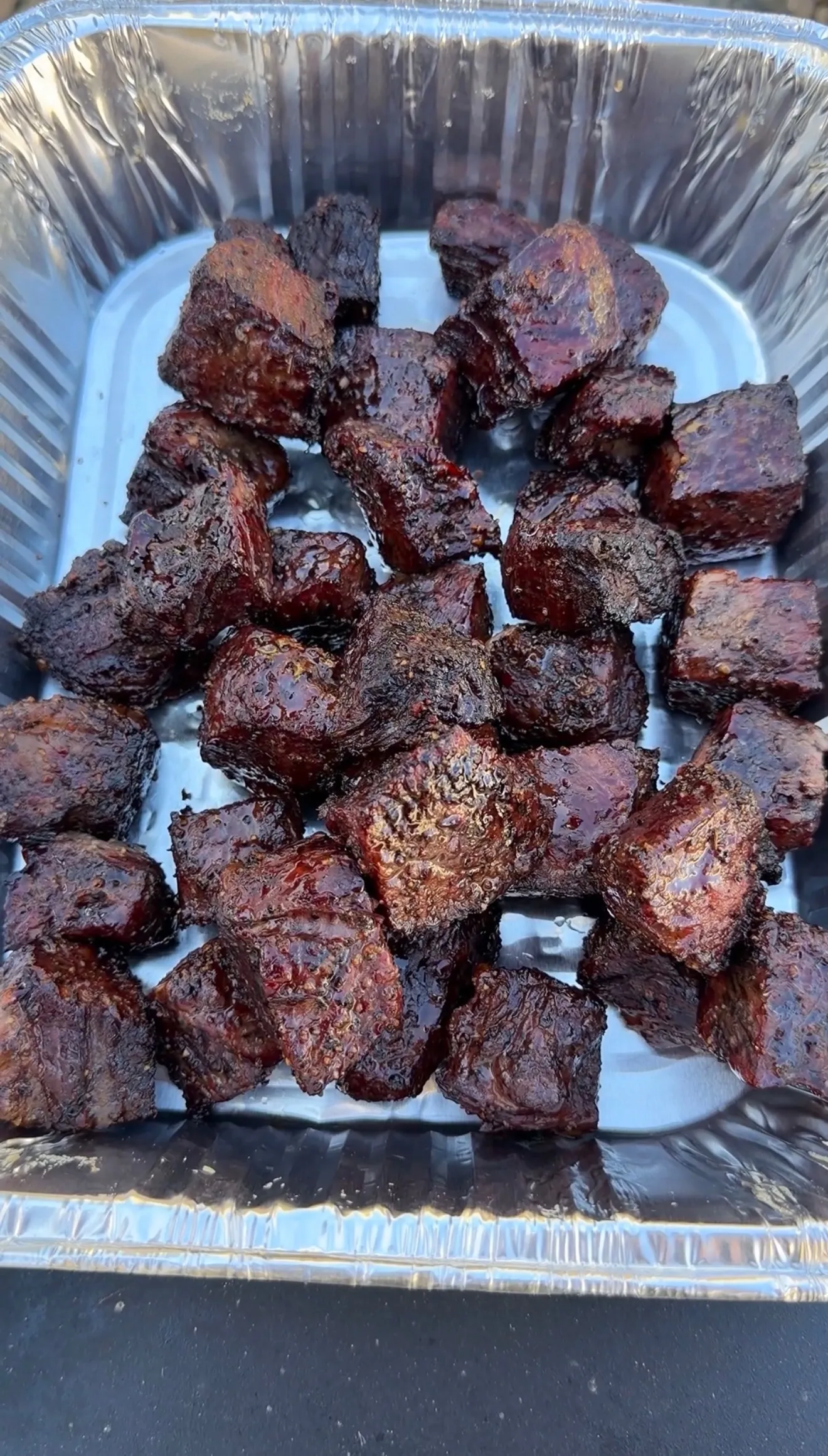 Dark caramelized smoked molasses coffee beef rib burnt ends arranged in aluminum foil pan