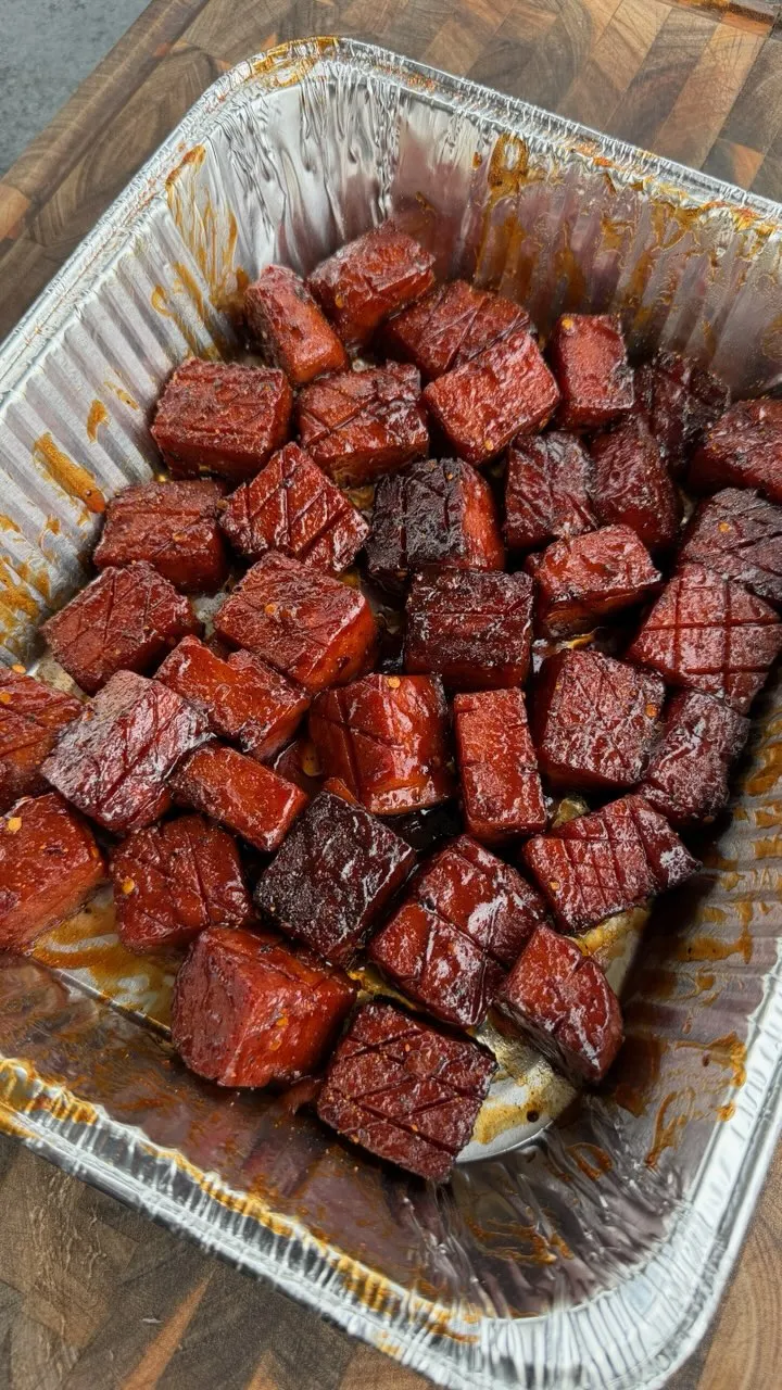 Caramelized spam burnt ends with sticky BBQ glaze in a disposable aluminum foil pan on a wooden cutting board