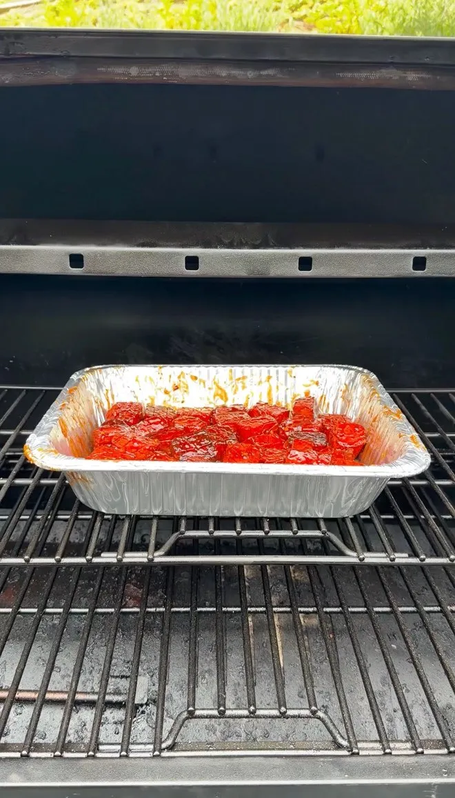 Glazed spam burnt ends in a disposable aluminum pan sitting on smoker grill grates