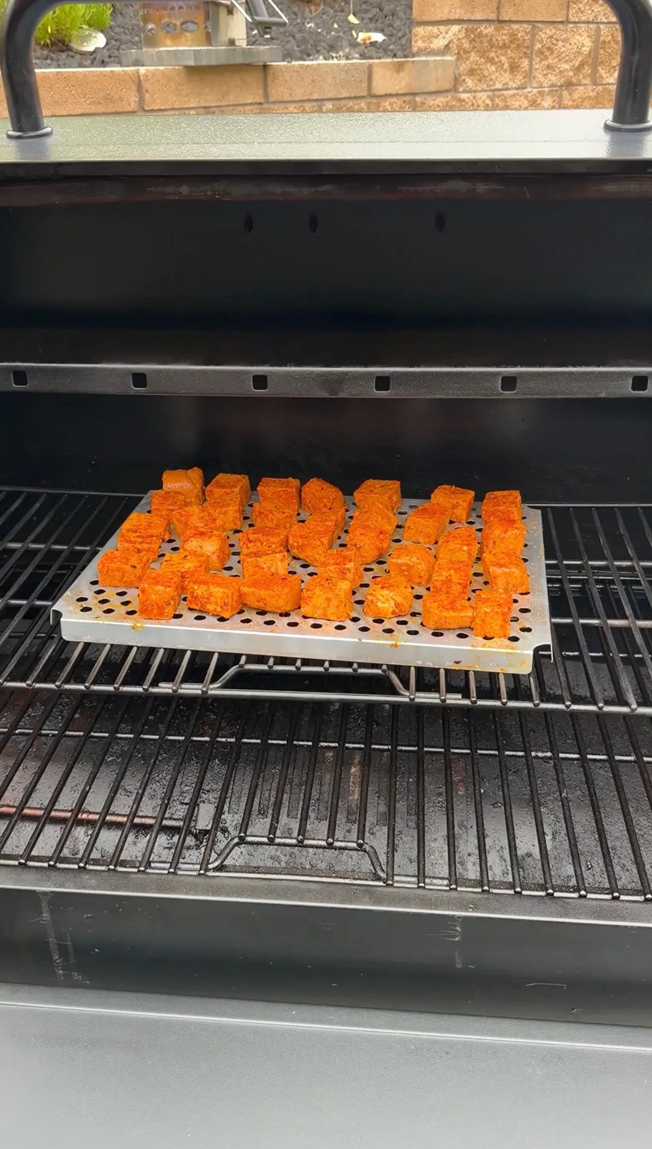 Seasoned spam cubes coated in red spice rub arranged on a perforated tray inside a pellet smoker grill