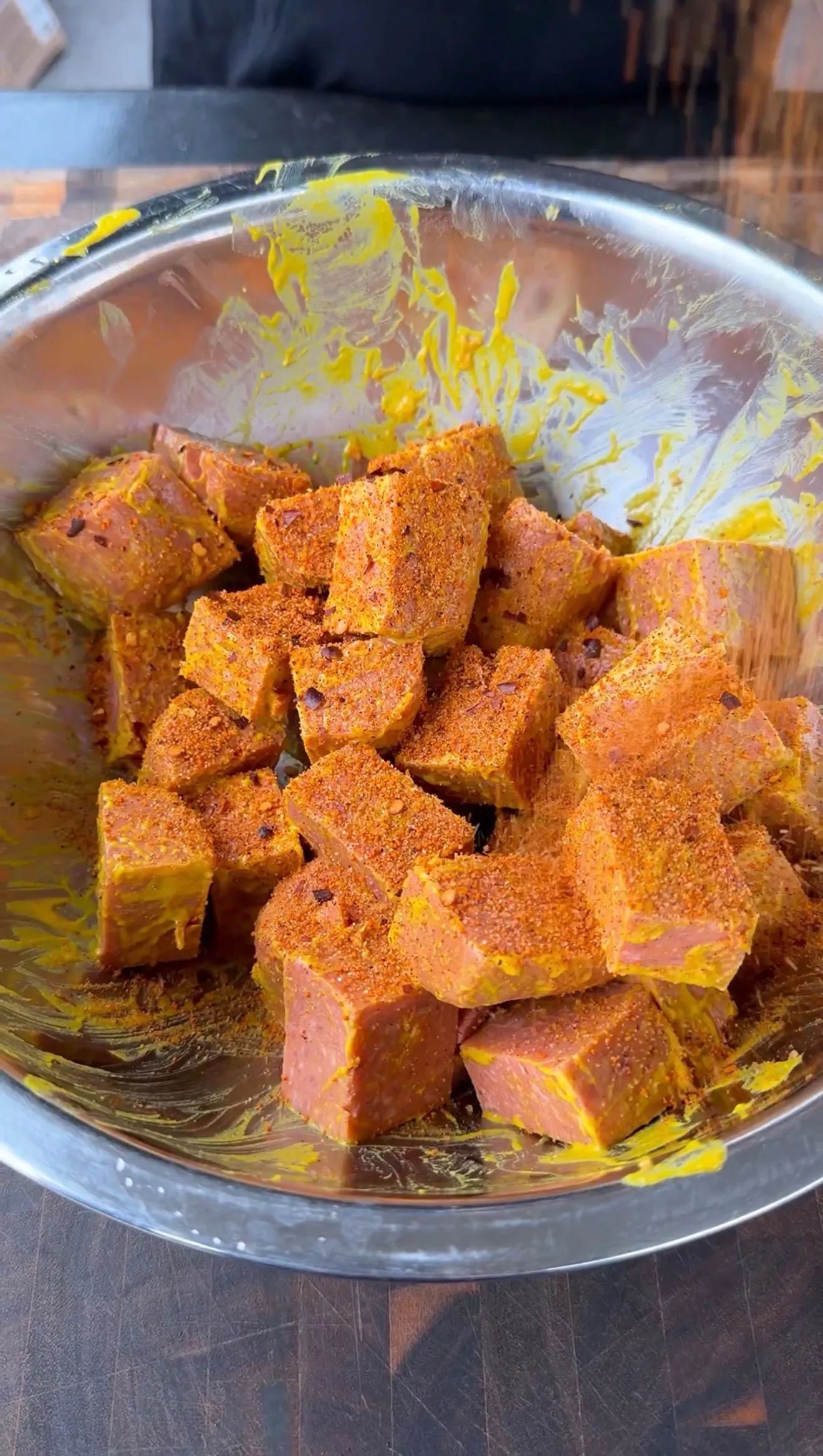 Cubed Spam pieces generously coated in orange-red spice rub in a stainless steel mixing bowl
