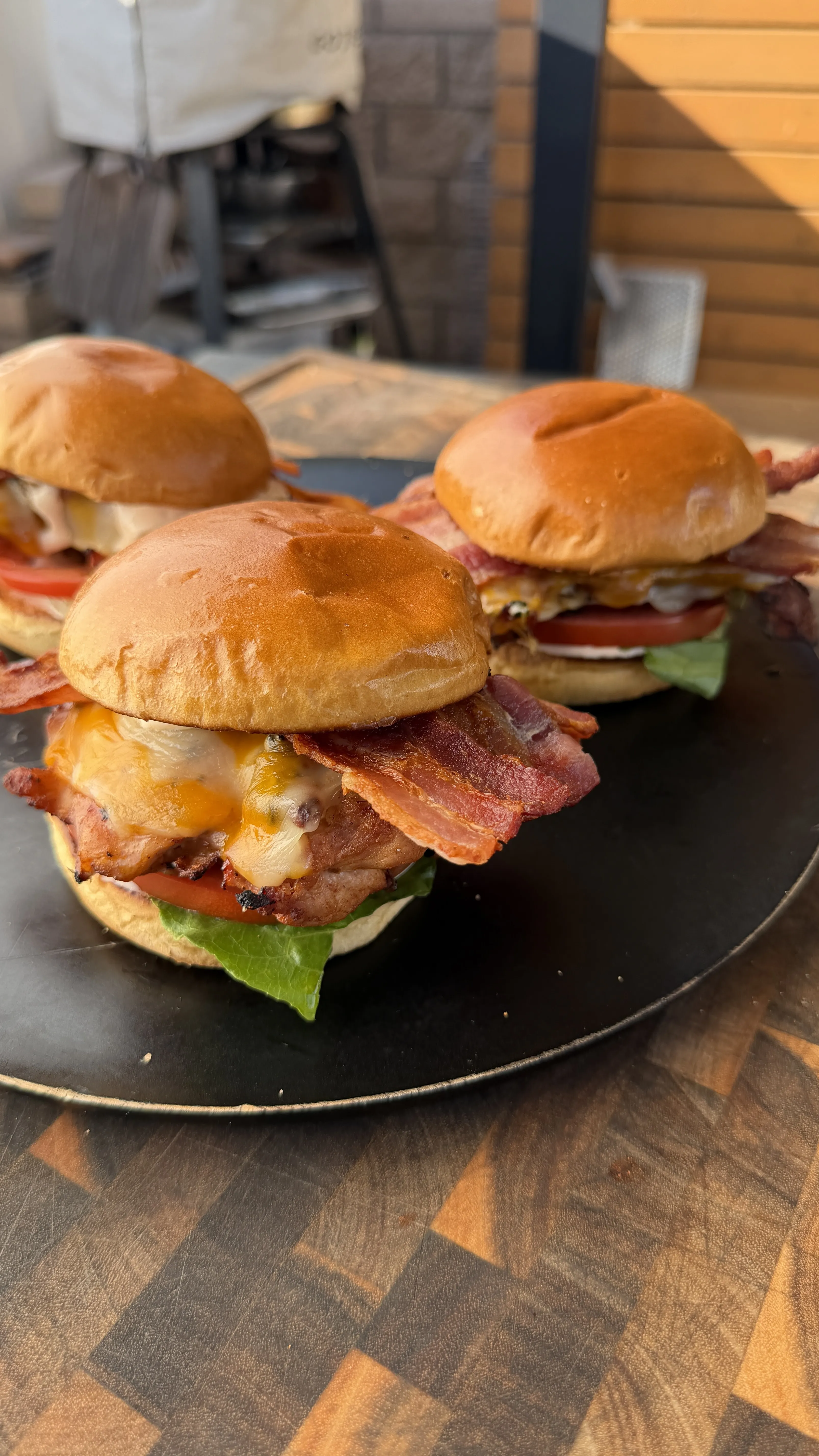 Three spicy chicken BLT sandwiches with crispy bacon, melted cheese, lettuce, and tomato on toasted brioche buns