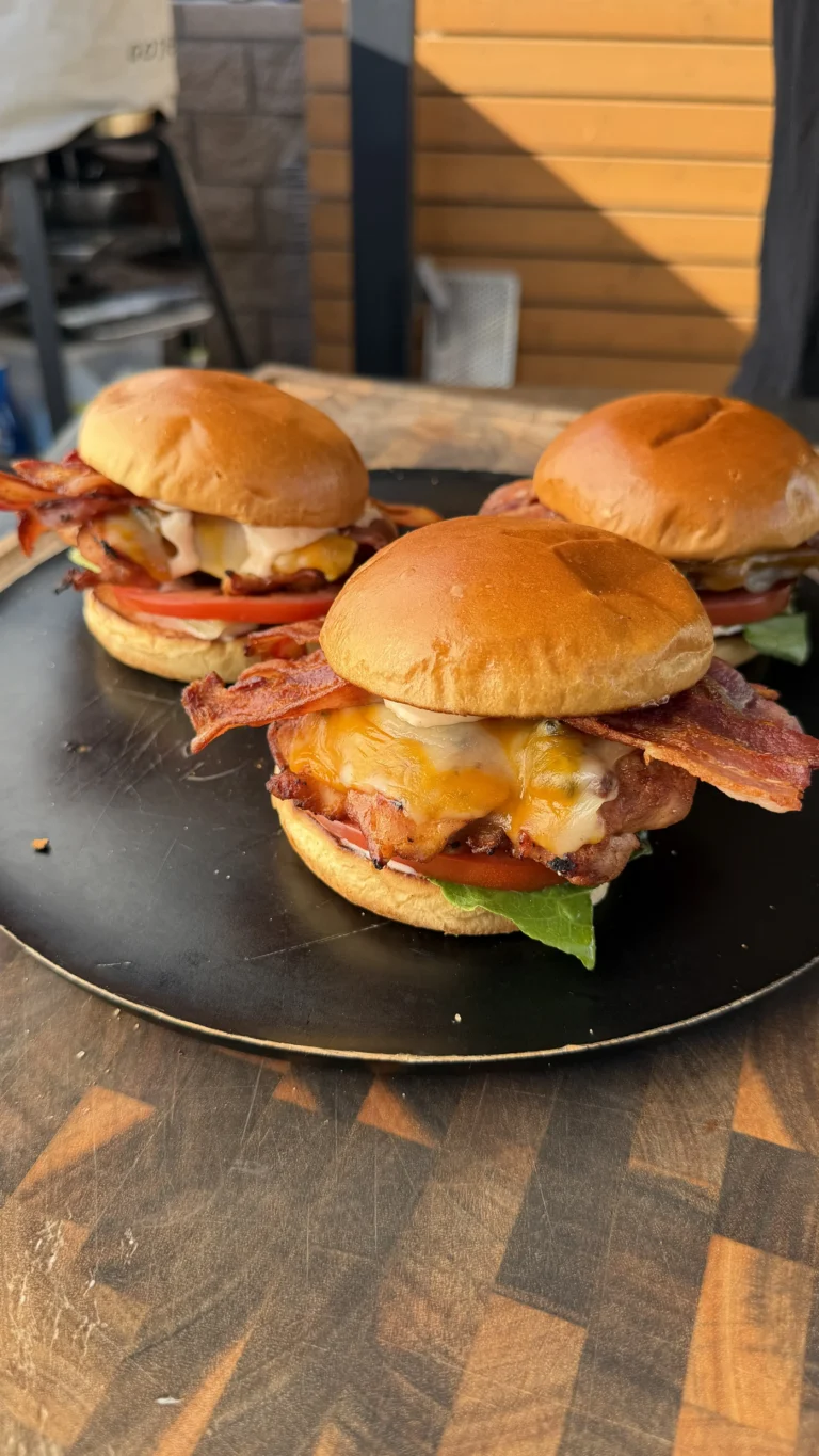 Three spicy chicken BLT sandwiches with melted cheddar, crispy bacon, tomato, and lettuce on a black plate