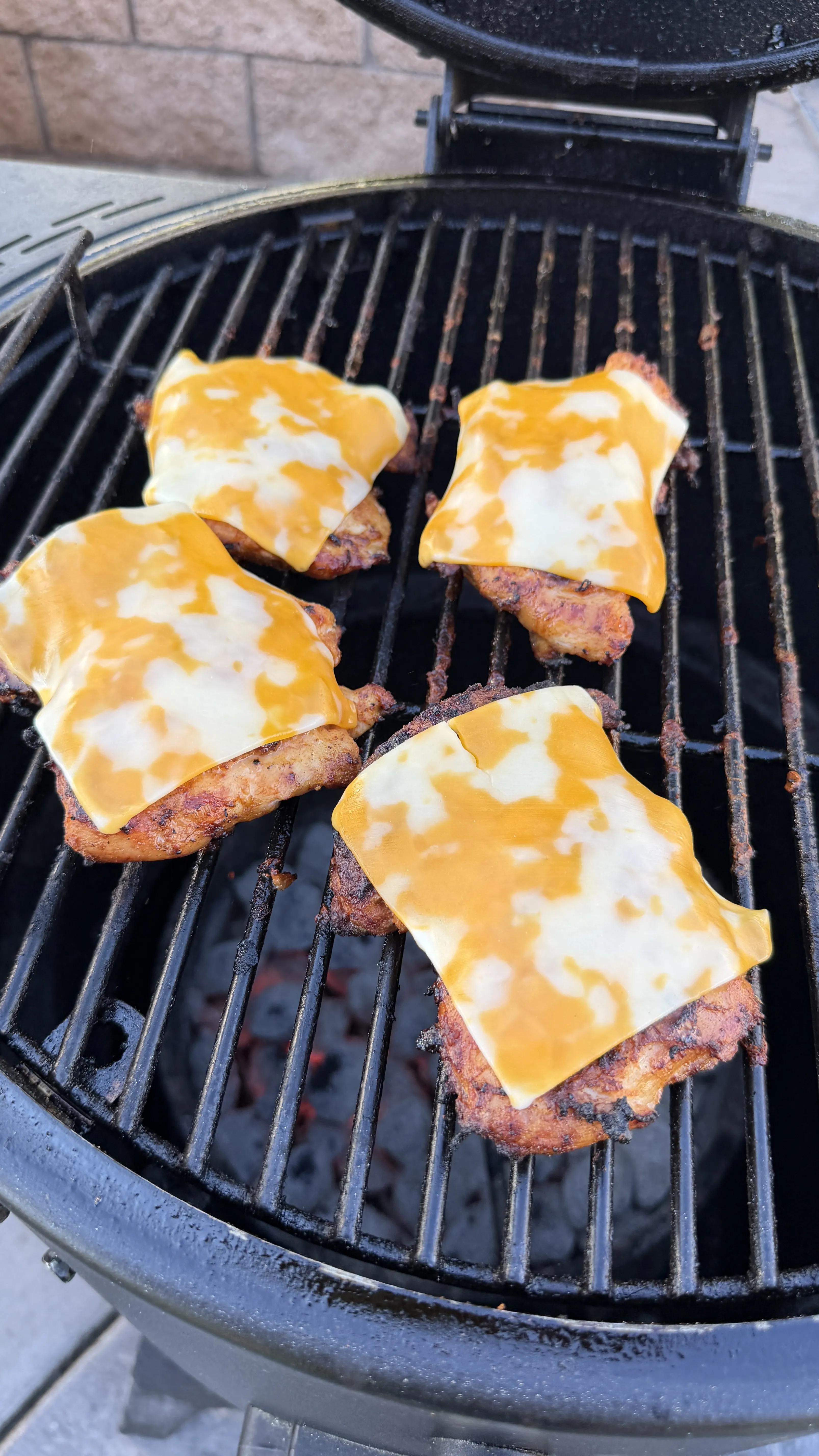 Seasoned chicken thighs topped with melting cheese grilling on a charcoal kamado-style grill