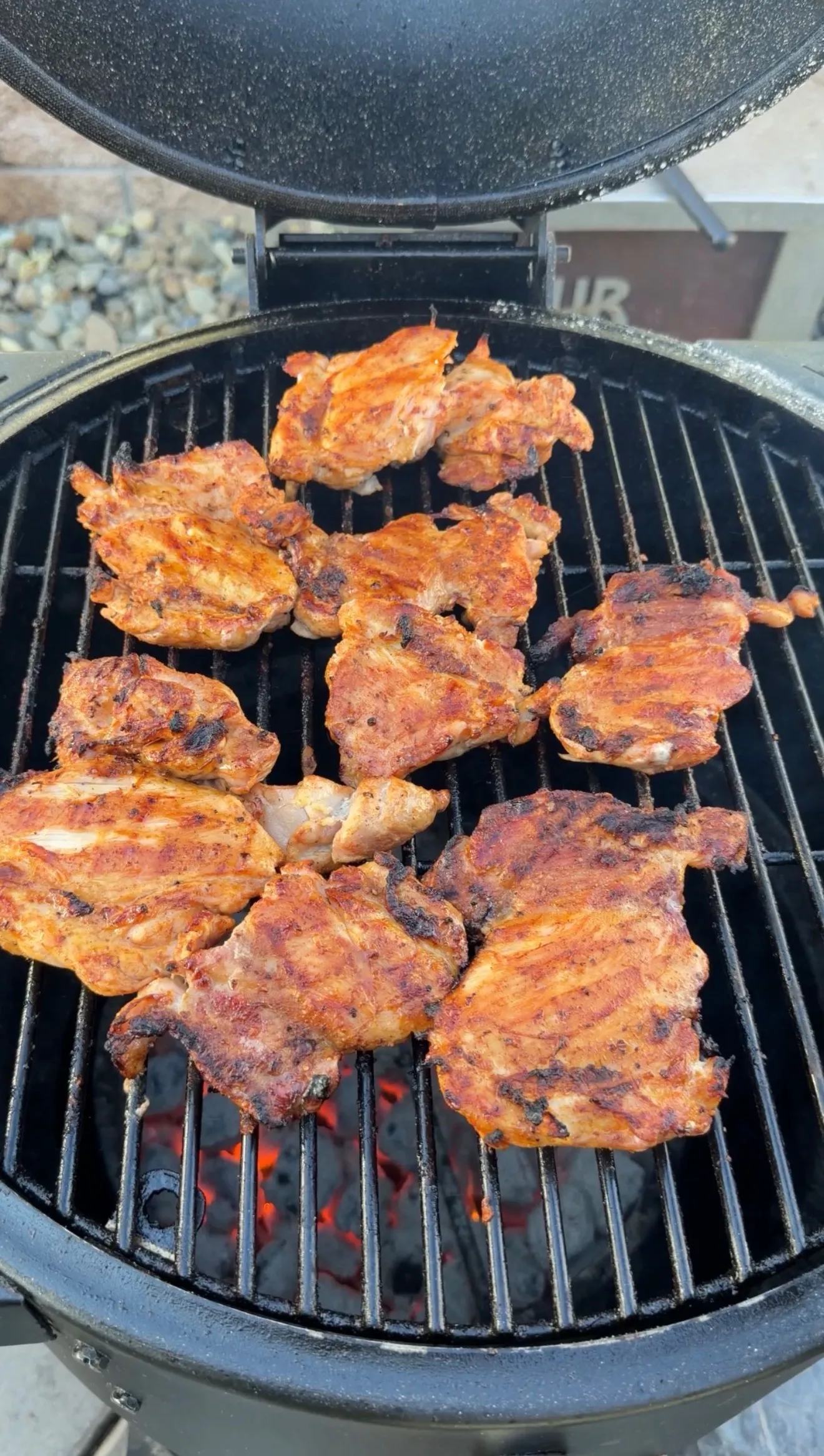 Marinated spicy chicken thighs grilling over hot charcoal on a round kamado-style BBQ grill