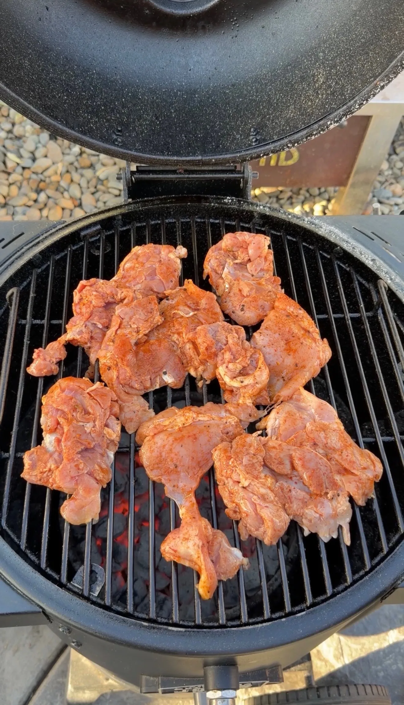 Spicy seasoned chicken thighs cooking on a charcoal kamado grill with glowing embers