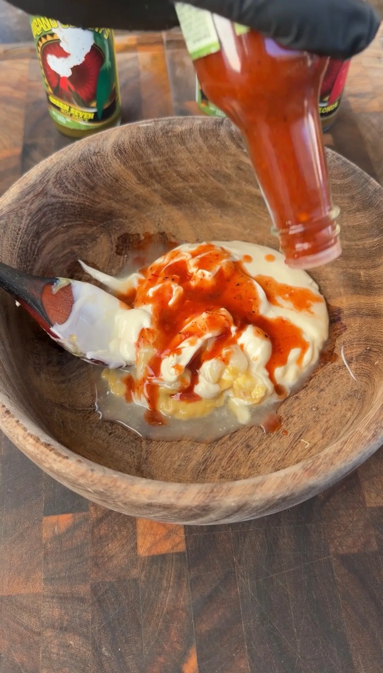 Hot sauce being poured over mayonnaise in a wooden bowl to make spicy aioli