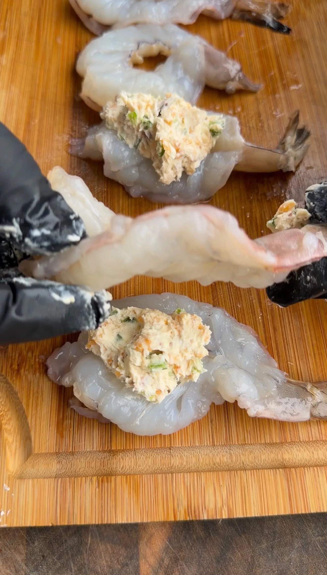Raw butterflied shrimp topped with jalapeño popper cream cheese filling on a wooden cutting board