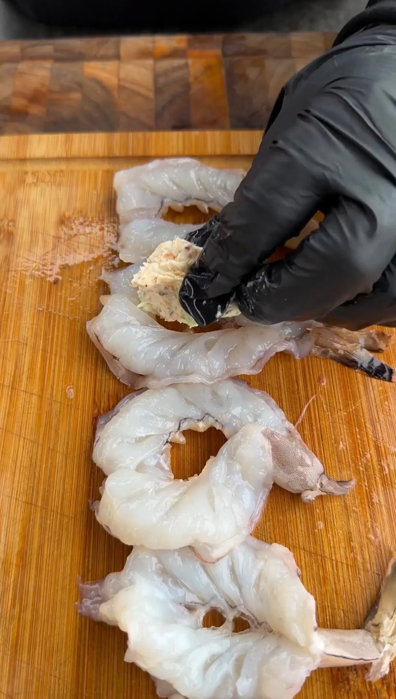 Gloved hands stuffing large raw shrimp with cream cheese jalapeño popper filling on a wooden cutting board
