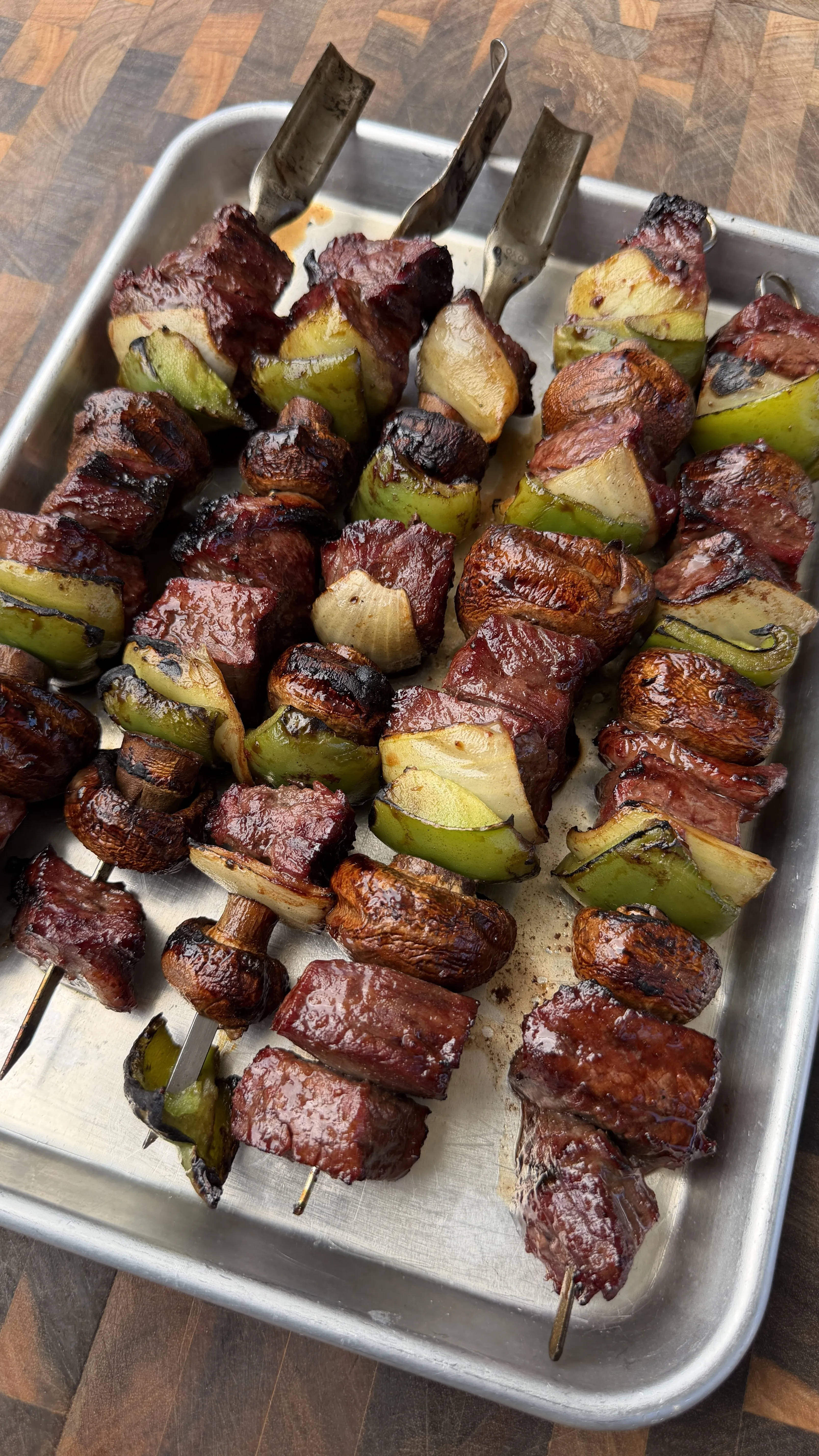 Grilled teriyaki beef skewers with peppers, onions and mushrooms on metal baking sheet
