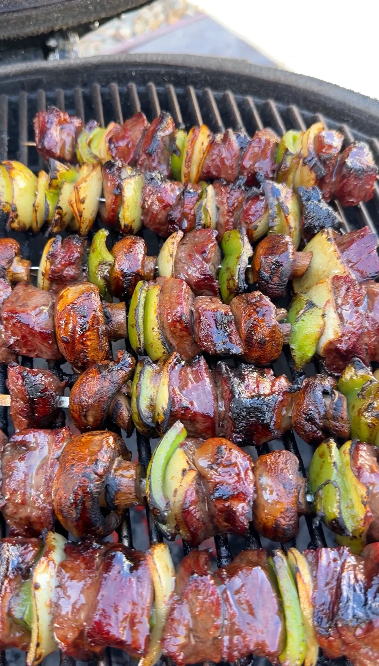 Teriyaki beef skewers with bell peppers and onions grilling on barbecue grill, being basted with sauce