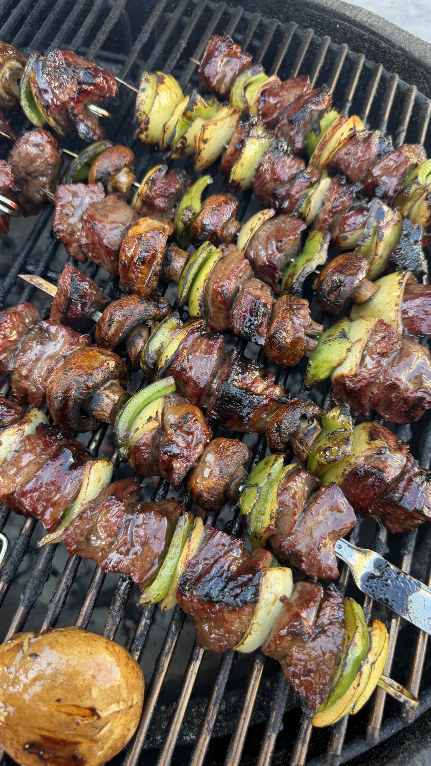 Teriyaki beef skewers with vegetables grilling on barbecue grates, showing caramelized glaze and char marks
