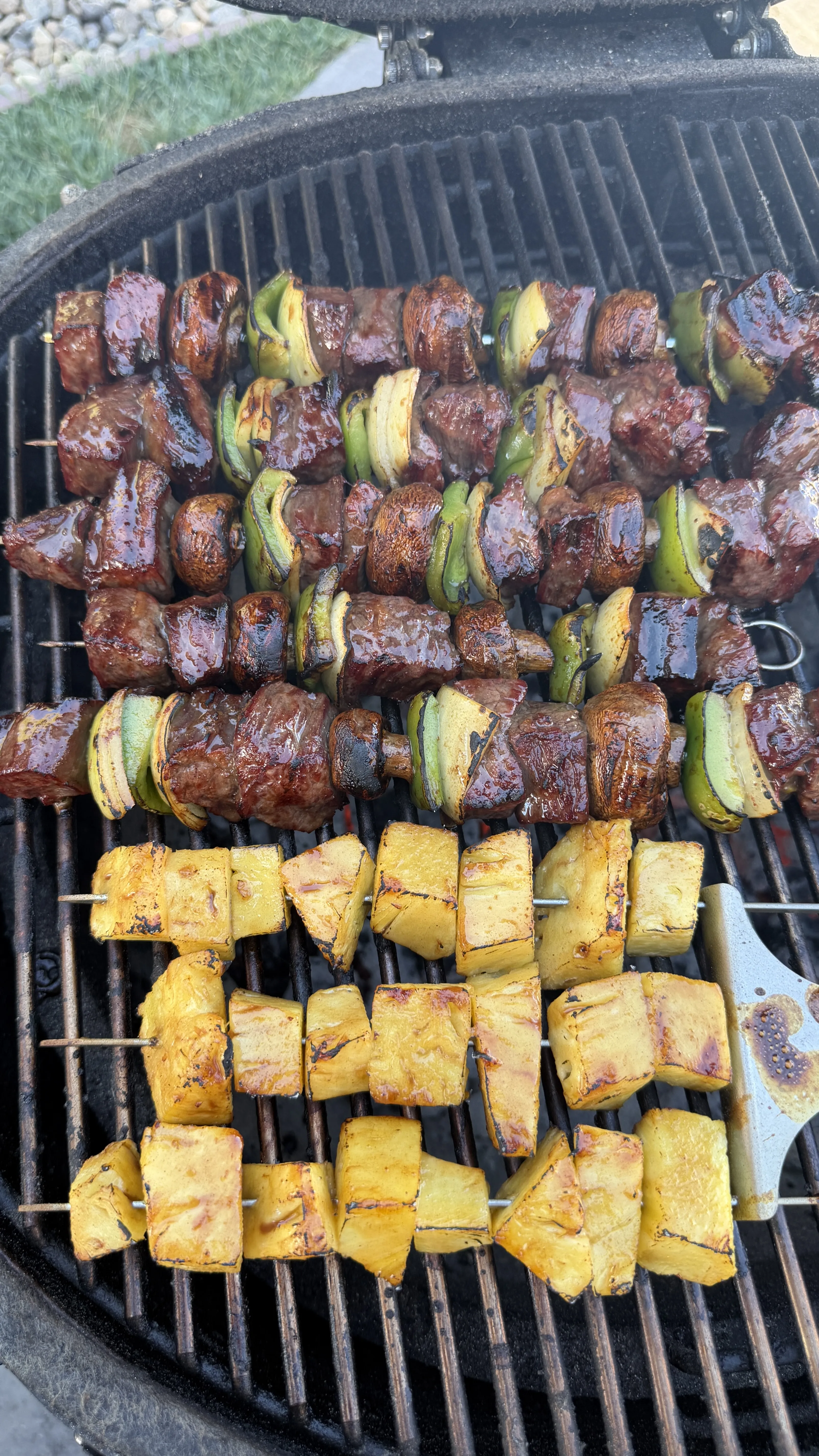 Teriyaki beef skewers with bell peppers grilling alongside pineapple chunks on outdoor barbecue grill