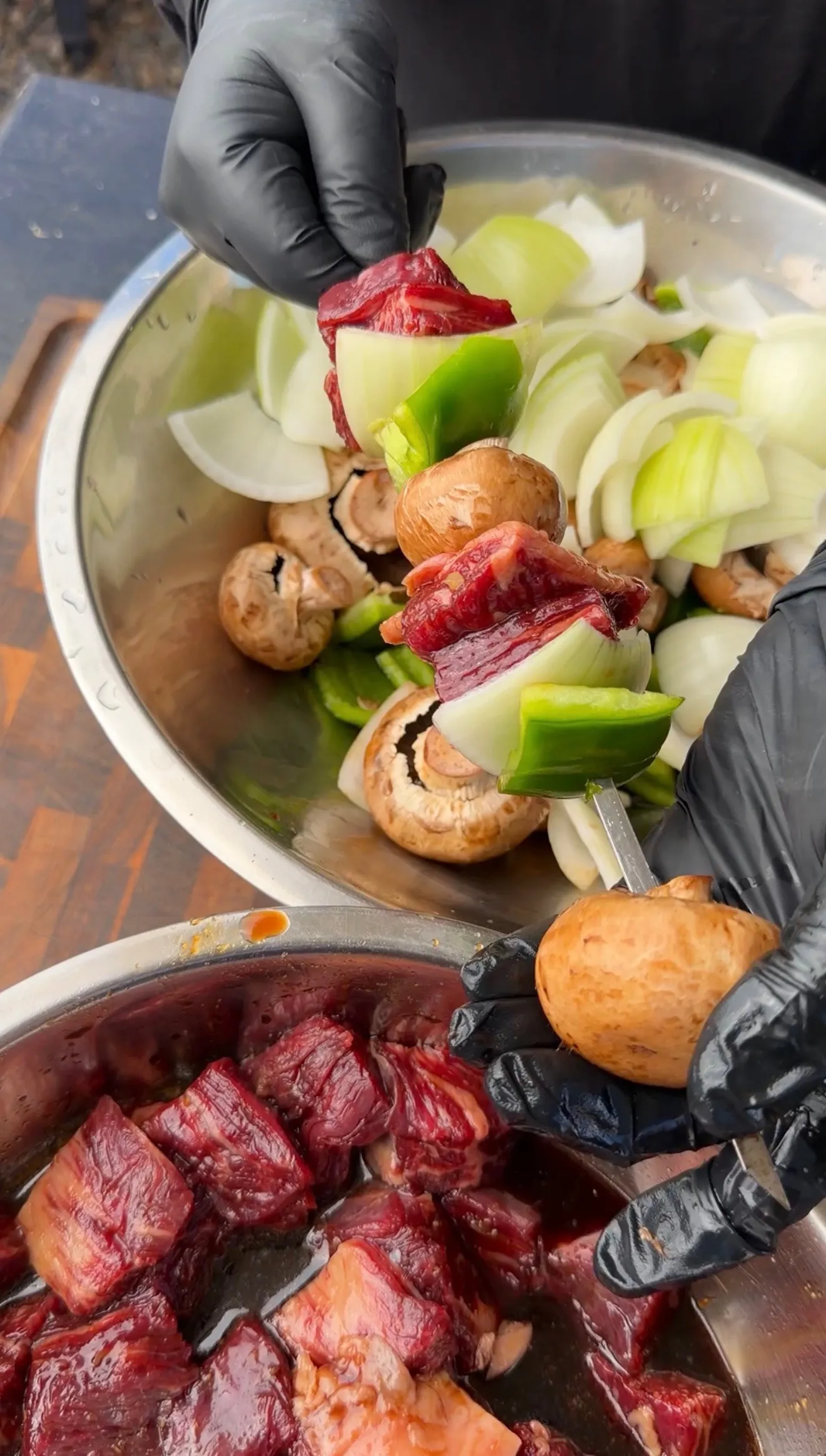 Raw marinated beef cubes and fresh vegetables being prepared for teriyaki skewers in metal bowls