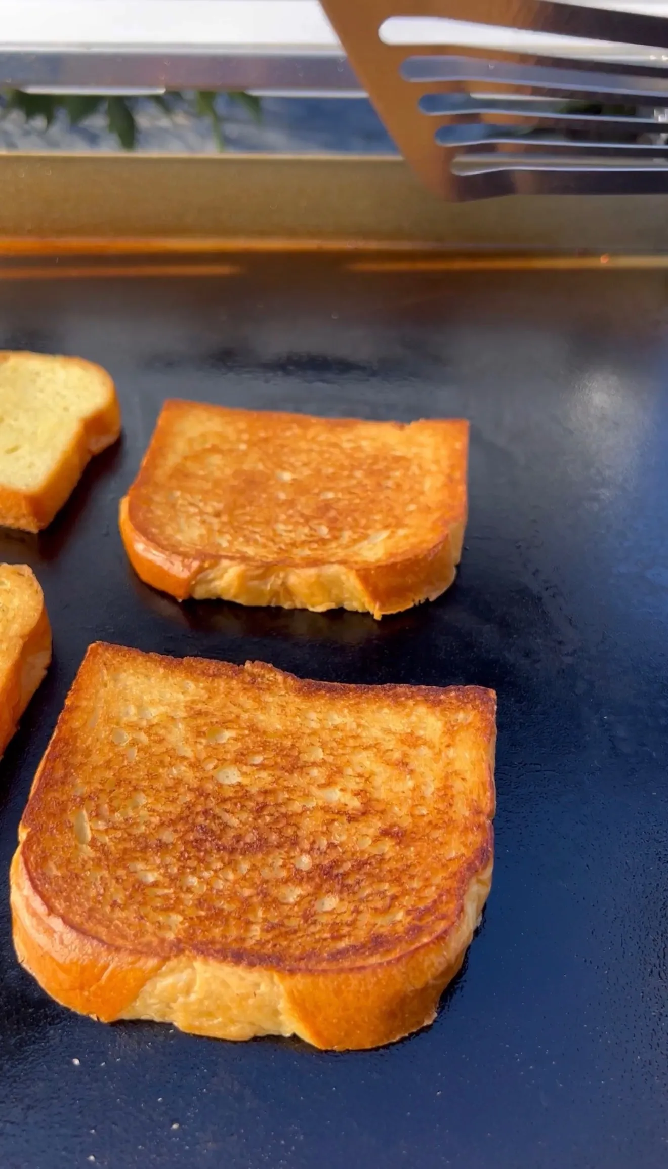 Golden brown toasted bread slices cooking on a dark griddle for avocado BLT sandwiches
