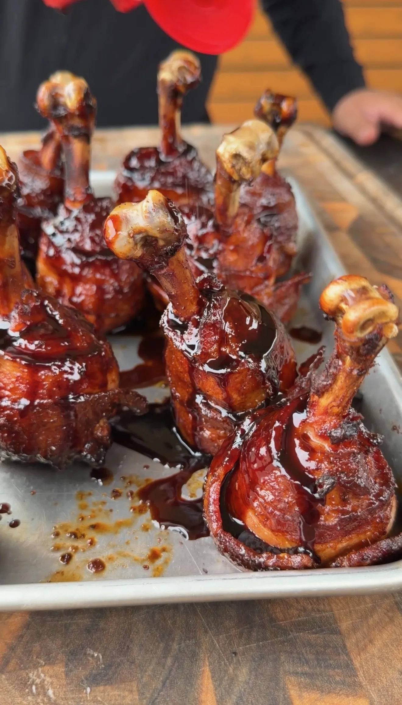 Bacon wrapped hot and spicy chicken lollipops glazed with dark BBQ sauce on a metal tray
