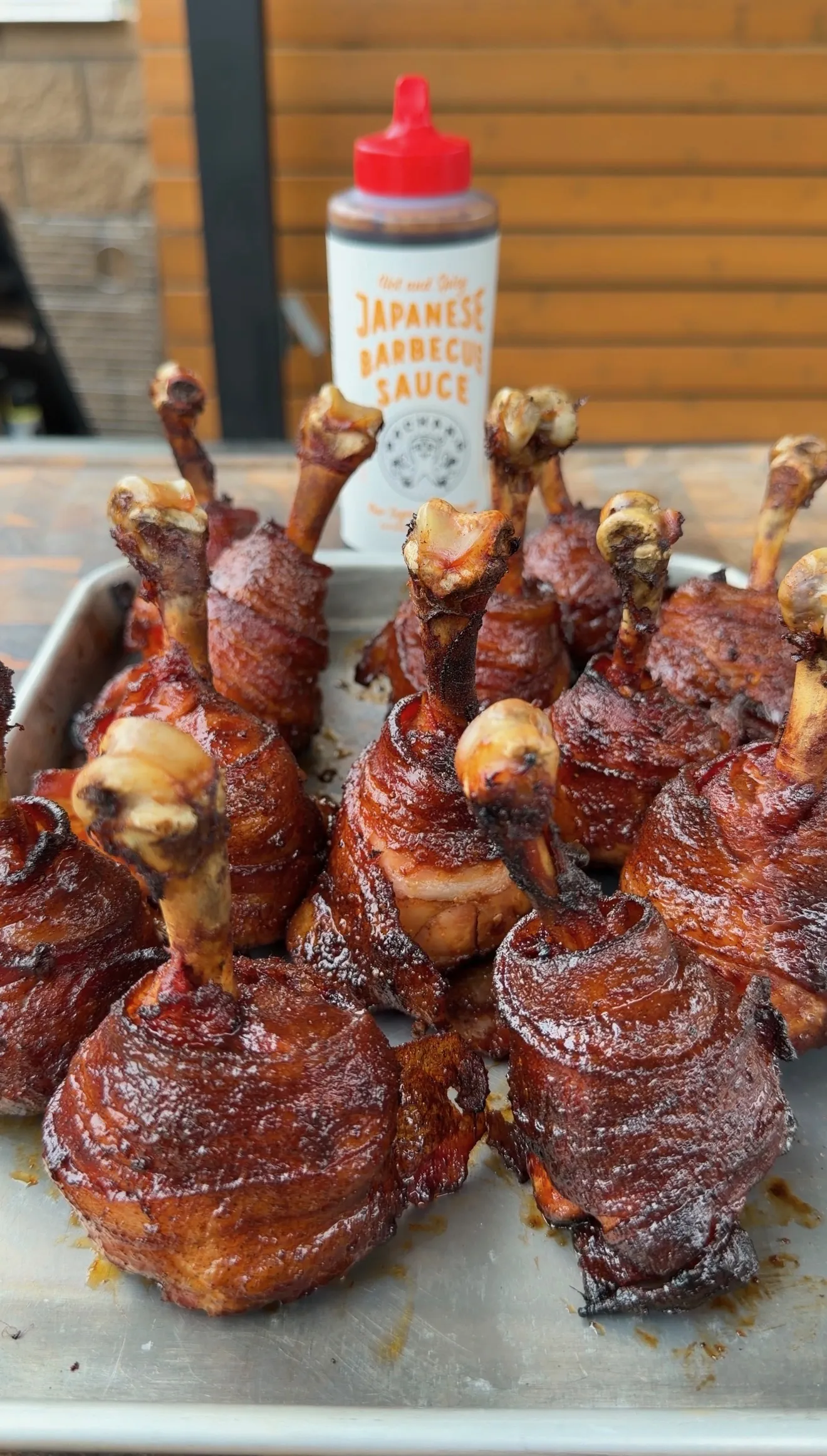Bacon-wrapped chicken lollipops glazed with hot and spicy Japanese BBQ sauce on a metal tray