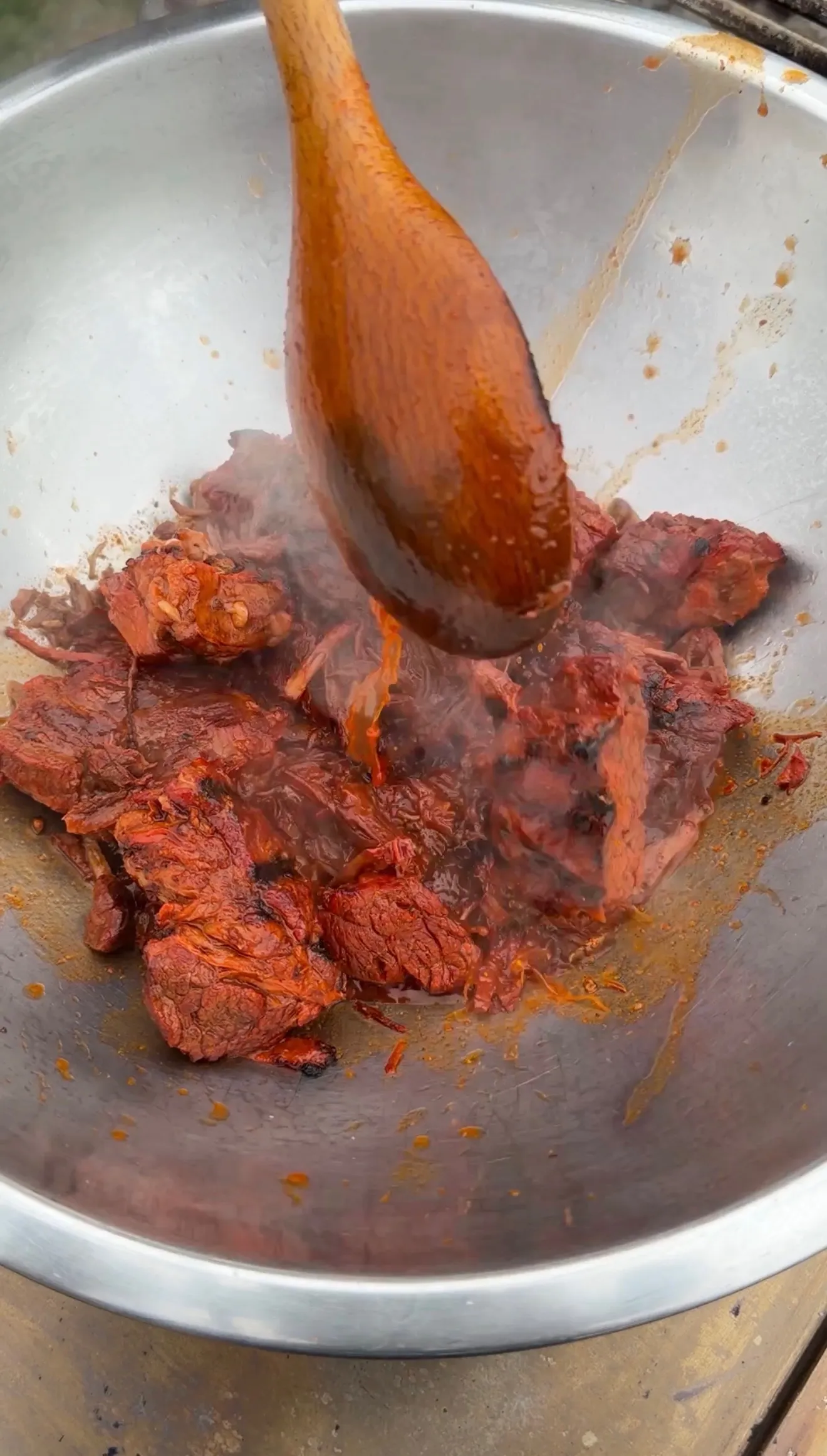 Tender birria beef chunks cooking in rich red chile sauce, stirred with a wooden spoon in a steel wok