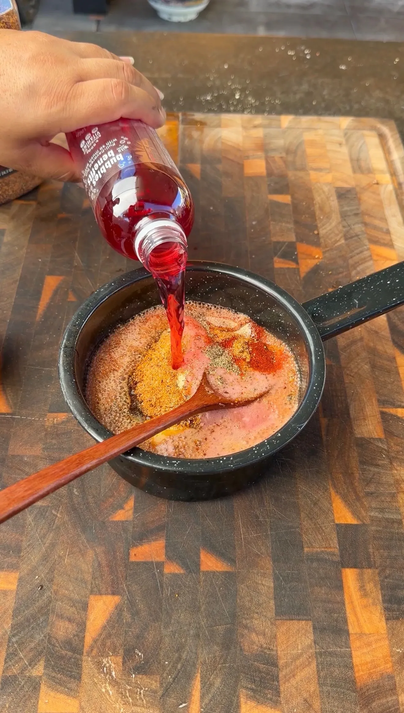 Pouring black raspberry juice into a black saucepan with spices to make BBQ sauce for smoked tomahawk pork chops