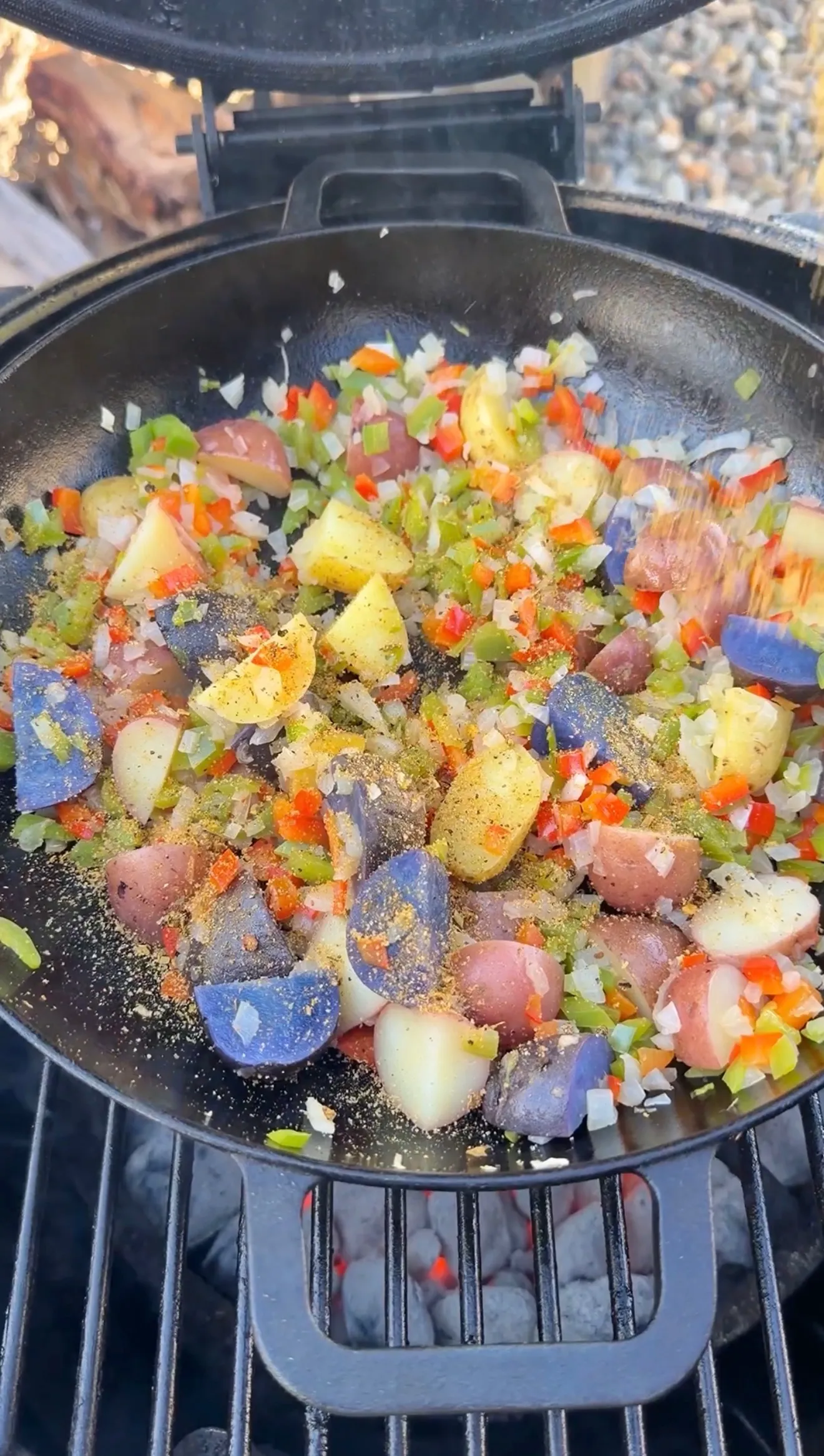 Colorful breakfast skillet with tri-color potatoes, diced red and green peppers, and onions seasoned with spices on a charcoal grill