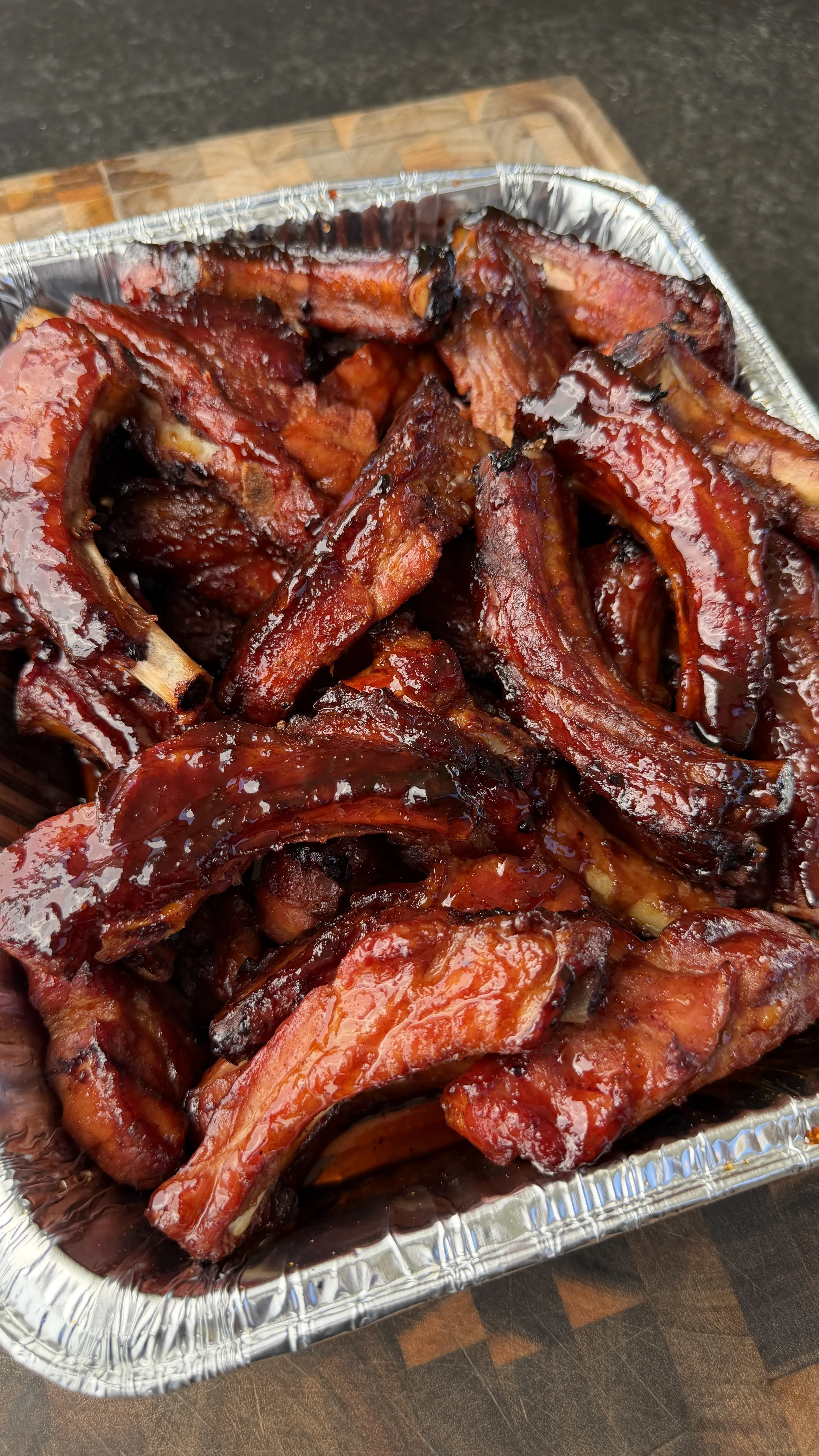 Glazed brown sugar bourbon party ribs piled high in a foil pan on a wooden cutting board