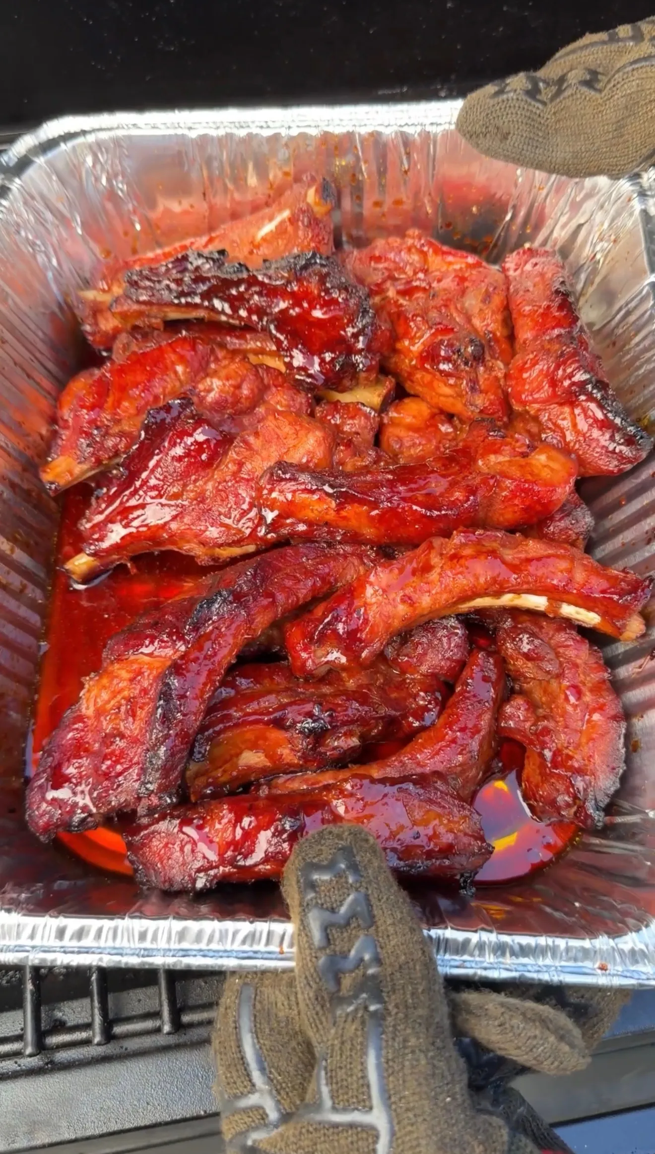 Saucy brown sugar bourbon party ribs piled in an aluminum pan with a glossy caramelized BBQ glaze