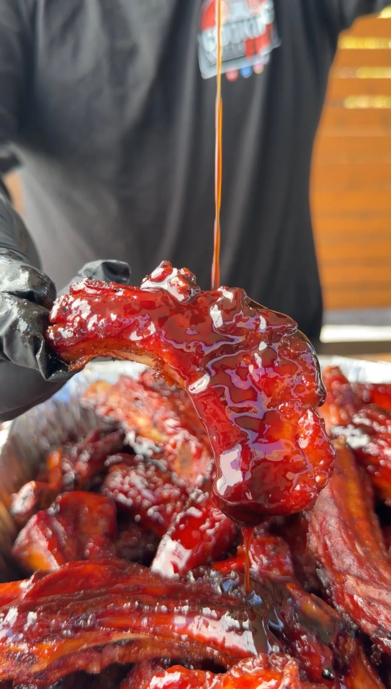 Glazed brown sugar bourbon party ribs being drizzled with sticky red BBQ sauce held in black gloved hand