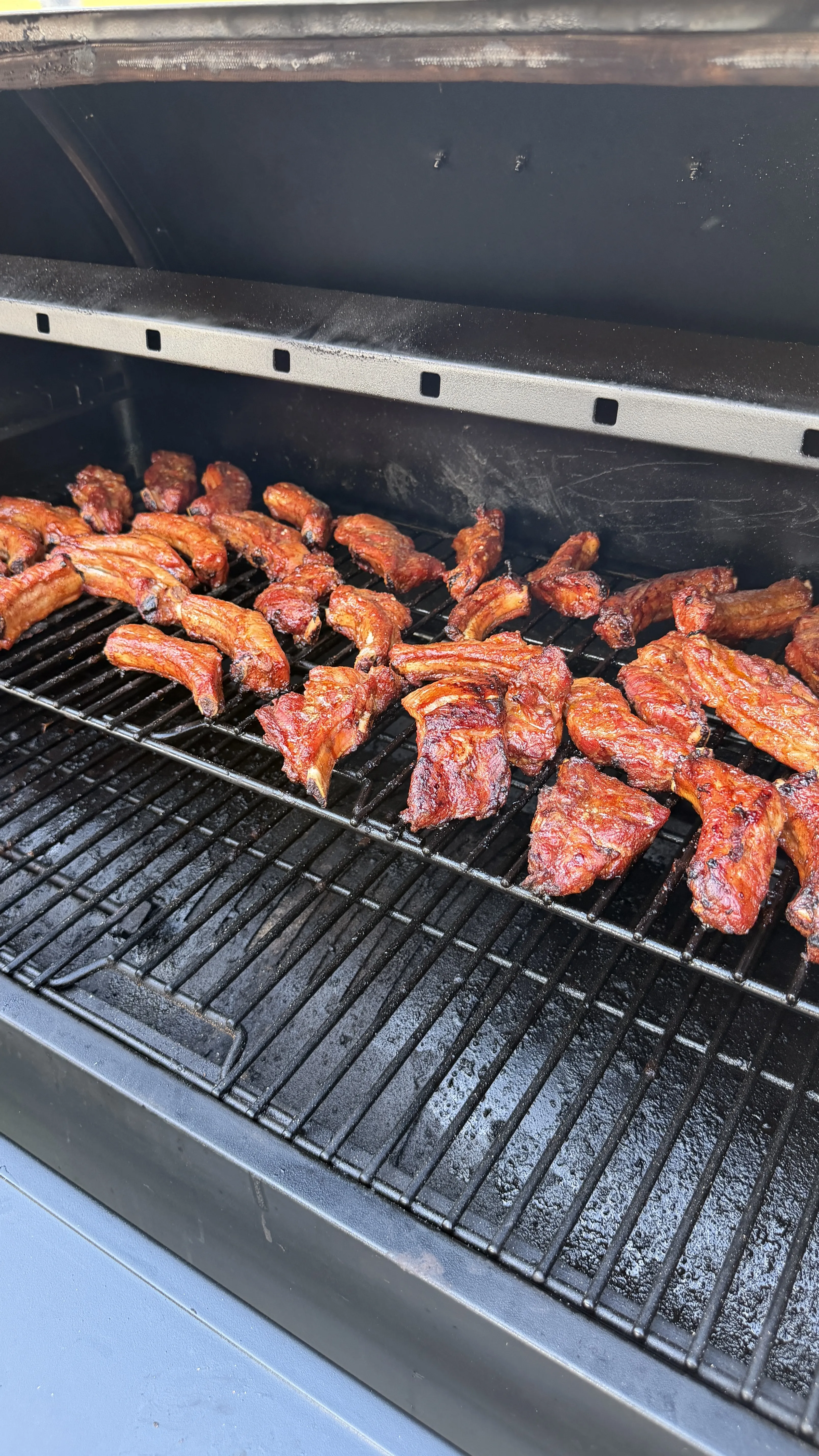 Brown sugar bourbon party ribs smoking on a large BBQ grill, glazed and caramelized to a deep mahogany color
