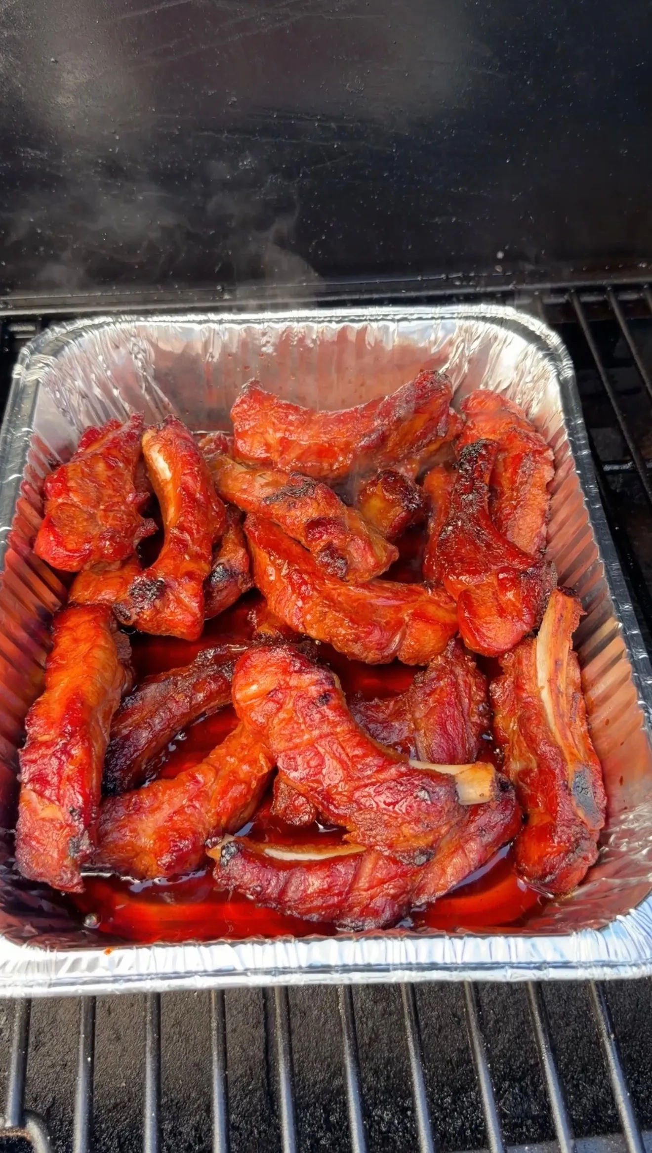 Glazed brown sugar bourbon party ribs in aluminum pan on smoker grill, coated in sticky red BBQ sauce