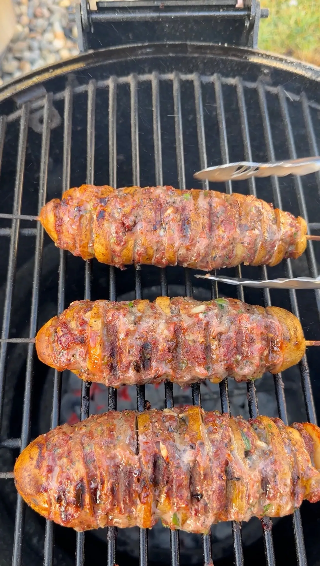 Three Cajun butter potato beef kebabs sizzling on a charcoal grill with tongs nearby