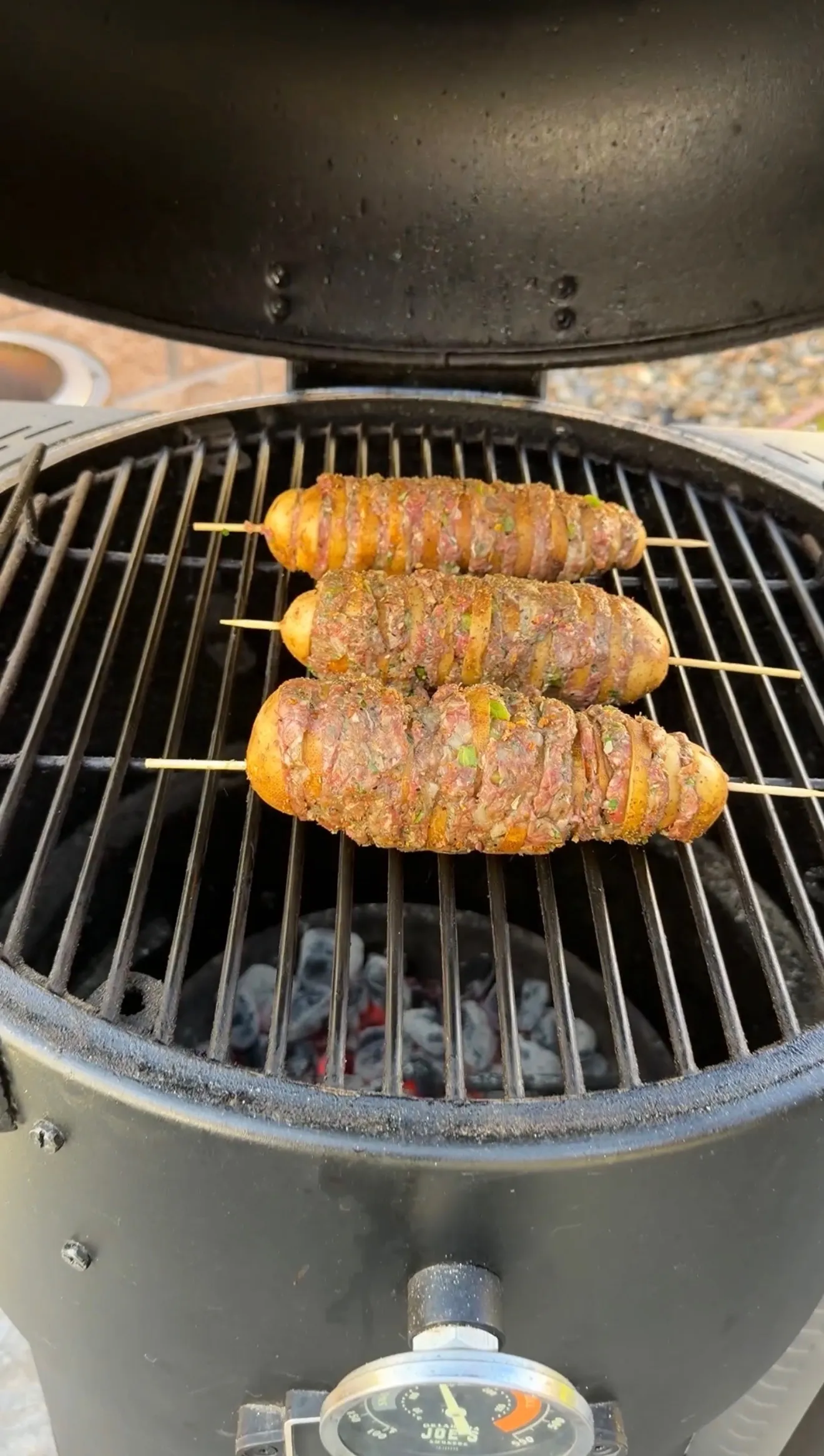 Three Cajun butter potato beef kebabs on skewers grilling over hot charcoal in a ceramic kamado grill