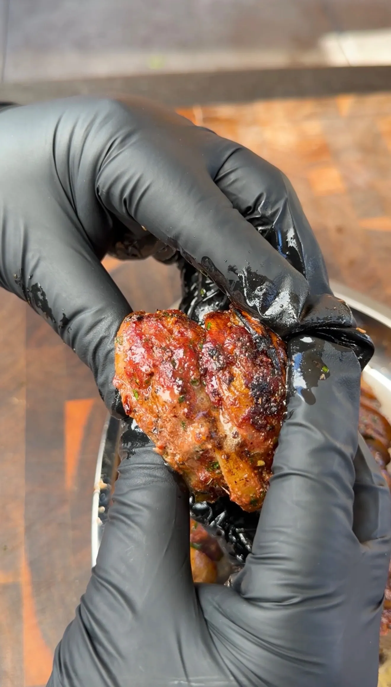 Hands in black gloves holding a glazed, charred Cajun butter beef kebab with herbs and caramelized crust