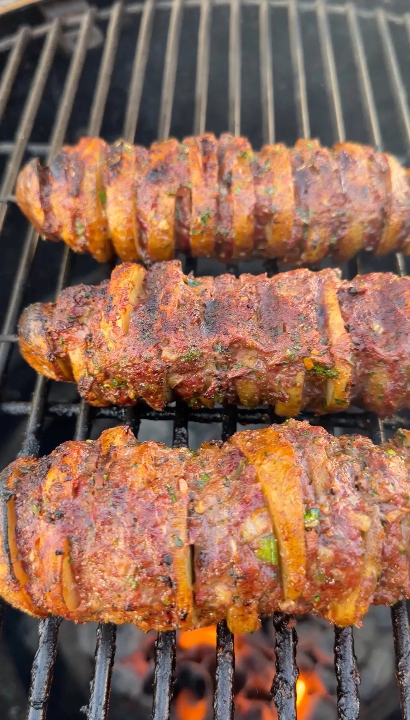 Three Cajun butter potato beef kebabs with spiced crust grilling over open flame on charcoal grill grates