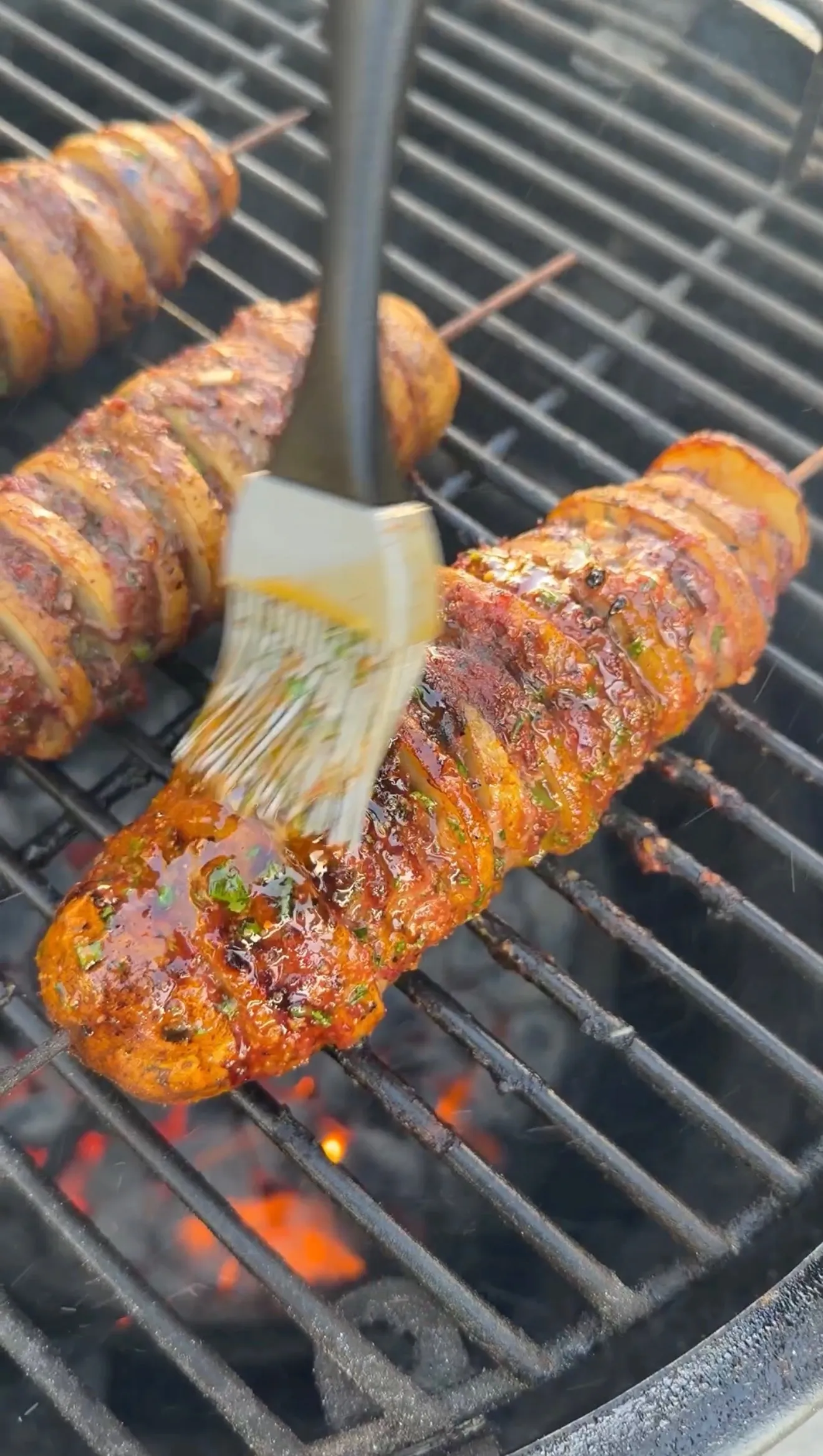 Cajun butter potato beef kebabs on charcoal grill being basted with spicy glaze using a silicone brush